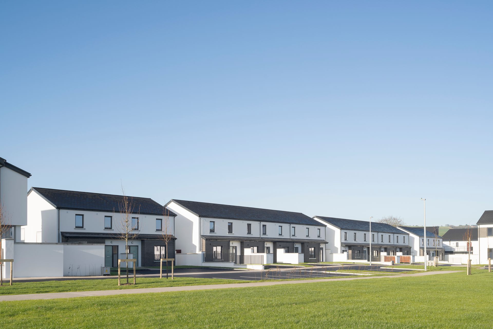 A row of white houses with black roofs are sitting next to each other on a lush green field.