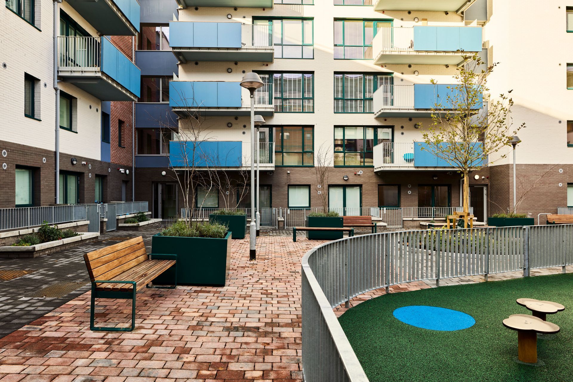 A brick courtyard with a bench and a playground in front of a building.