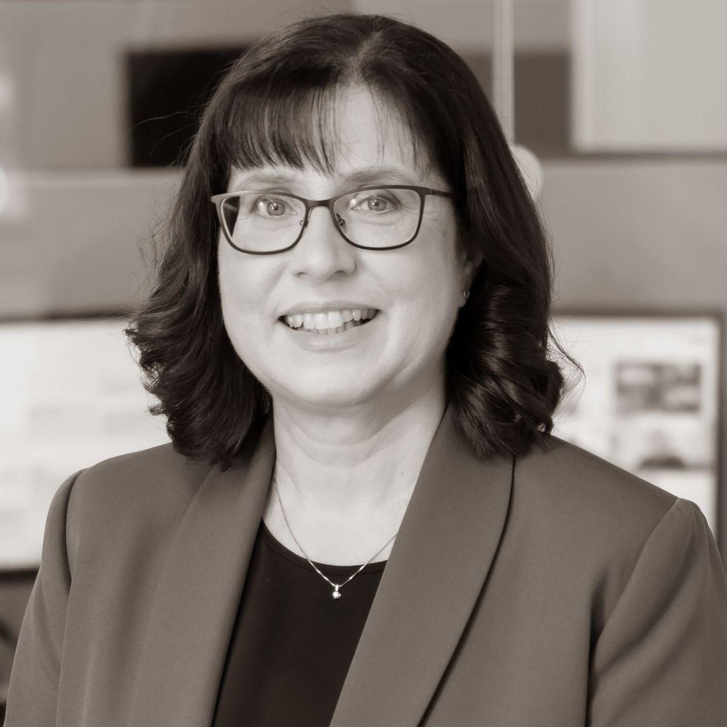 A woman wearing glasses and a jacket is smiling in a black and white photo.