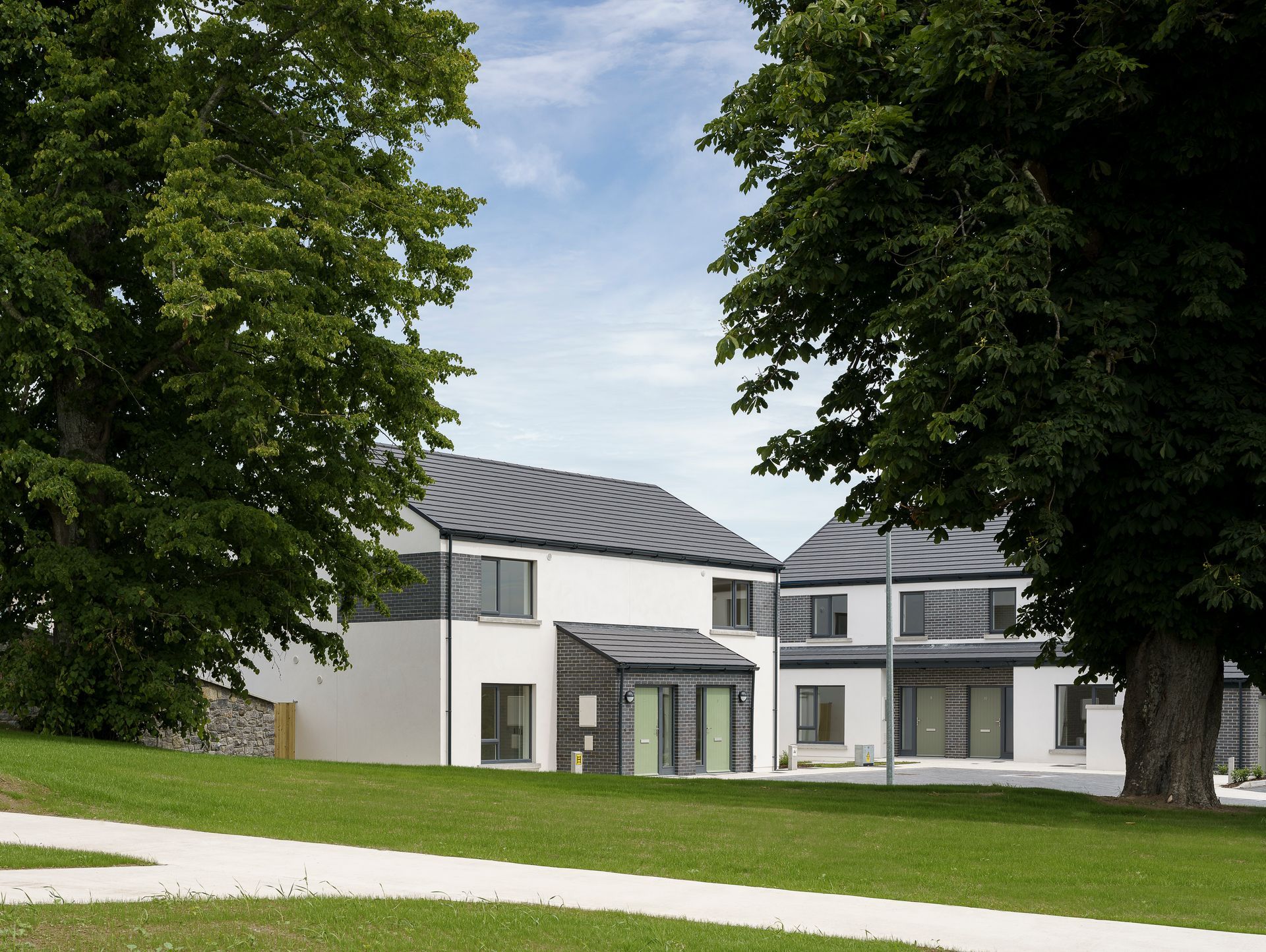 A white house with a black roof is surrounded by trees