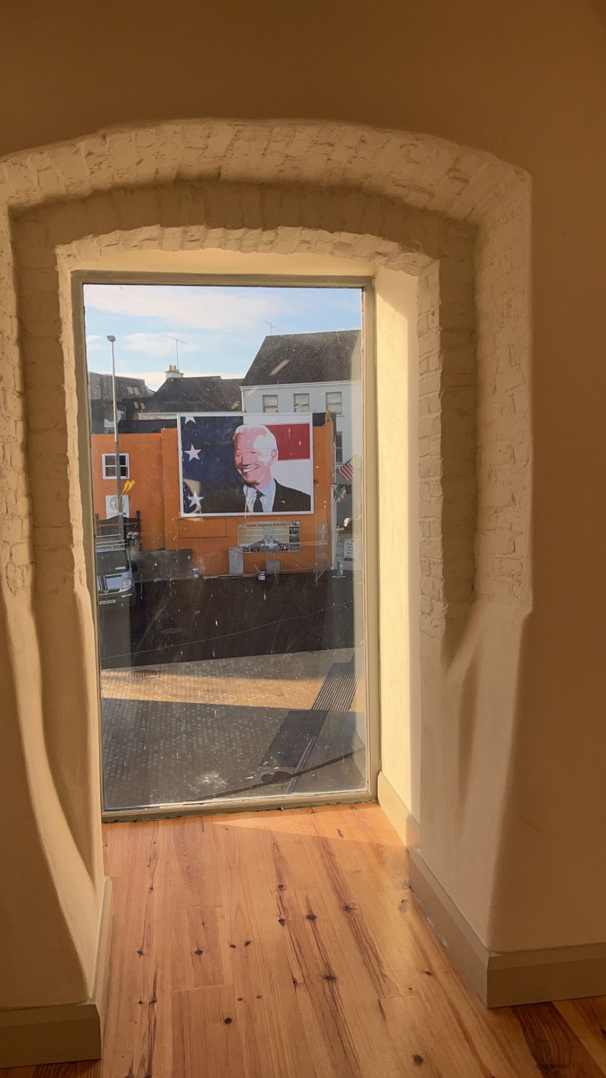 A room with a wooden floor and a window with a view of a building.