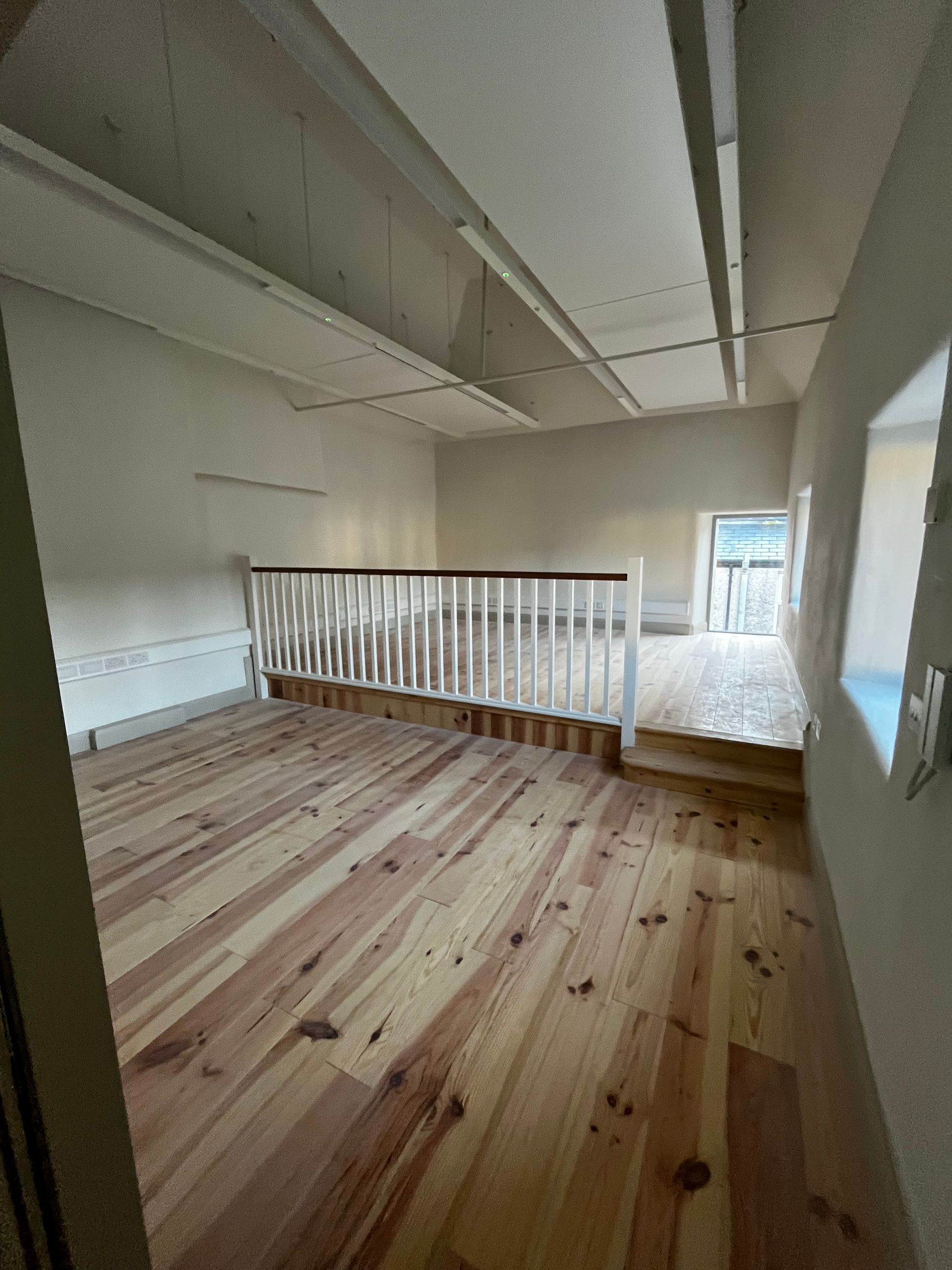 An empty room with wooden floors and a white railing