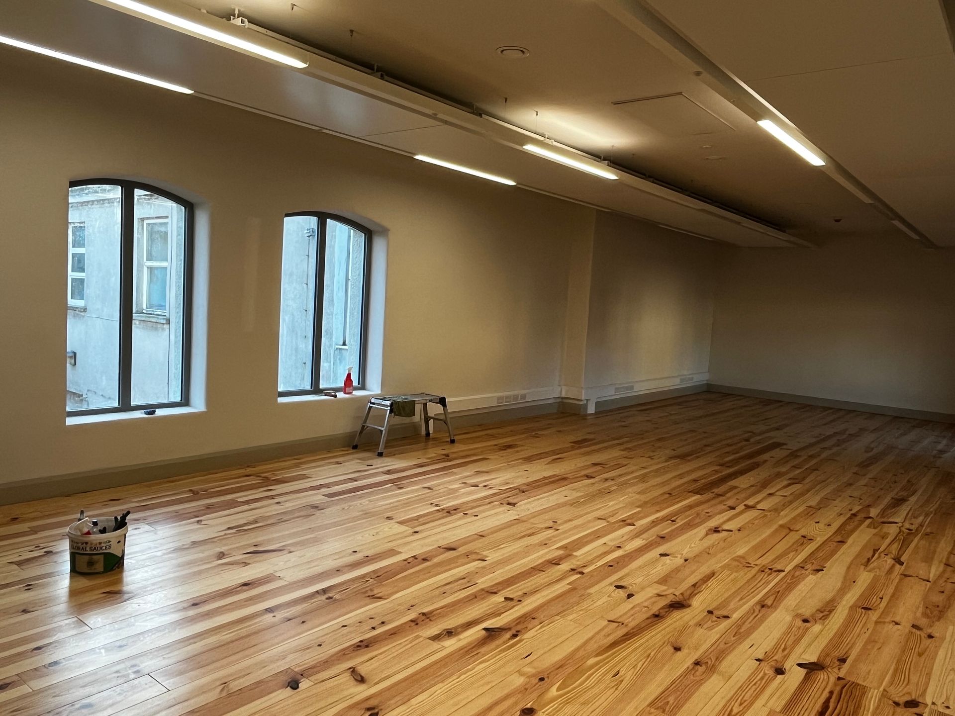 A large empty room with wooden floors and windows.