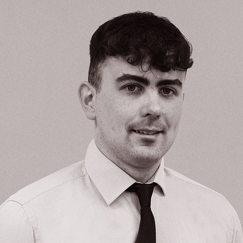 A man in a white shirt and black tie is smiling in a black and white photo.