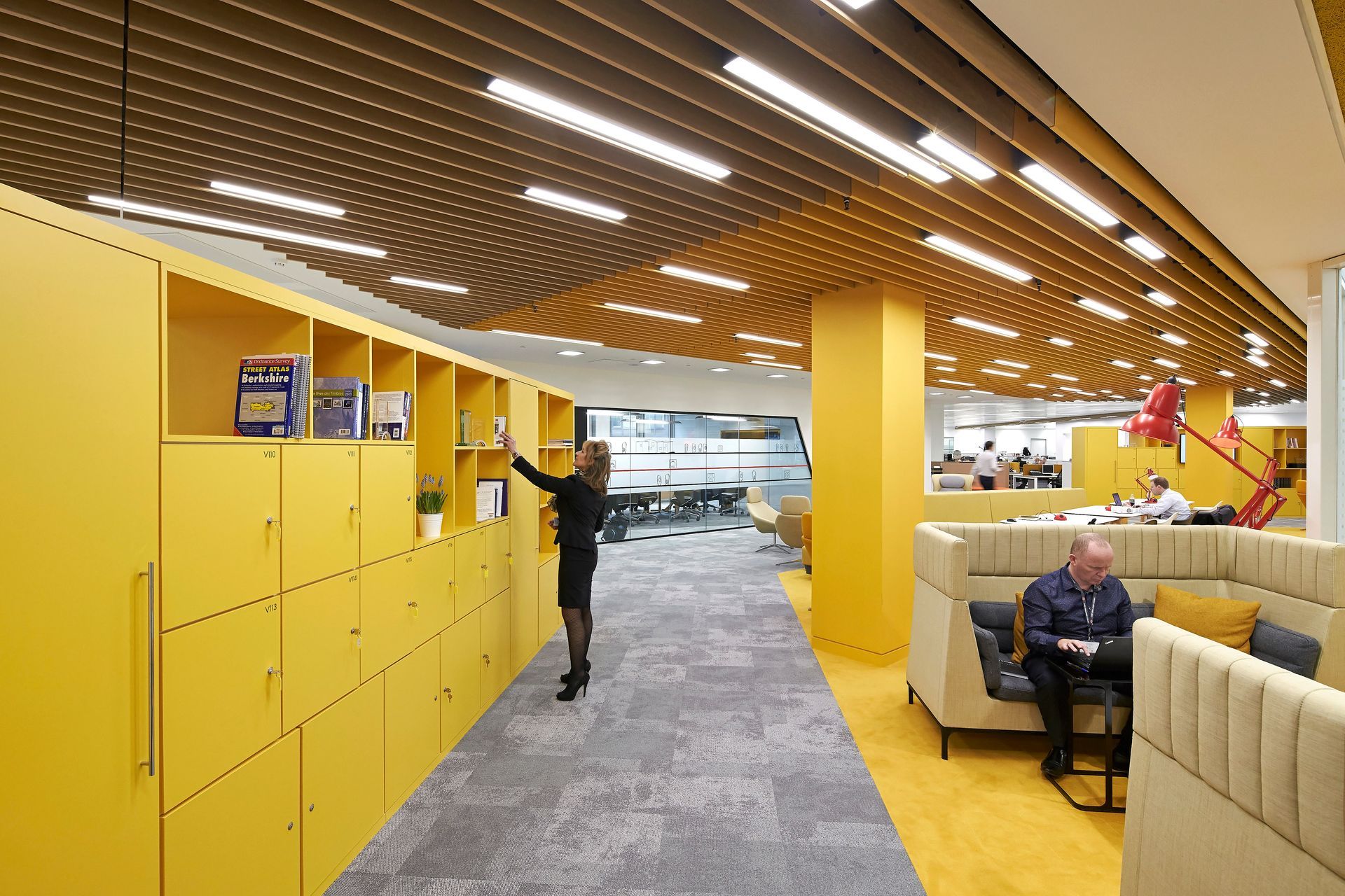 A man is sitting on a couch in a room with yellow lockers.