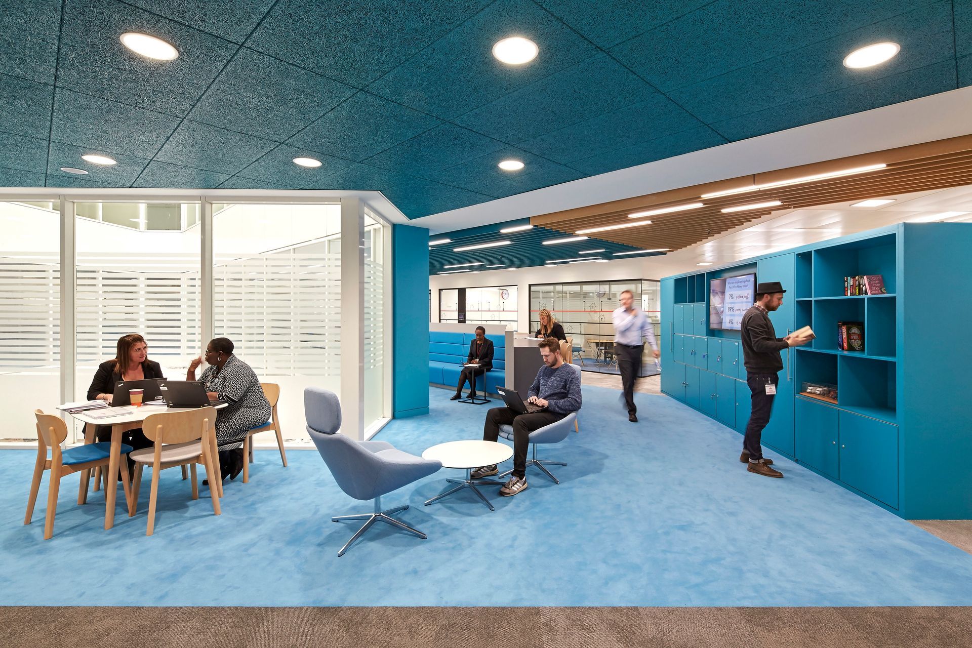 A group of people are sitting at tables in a room with blue carpet.