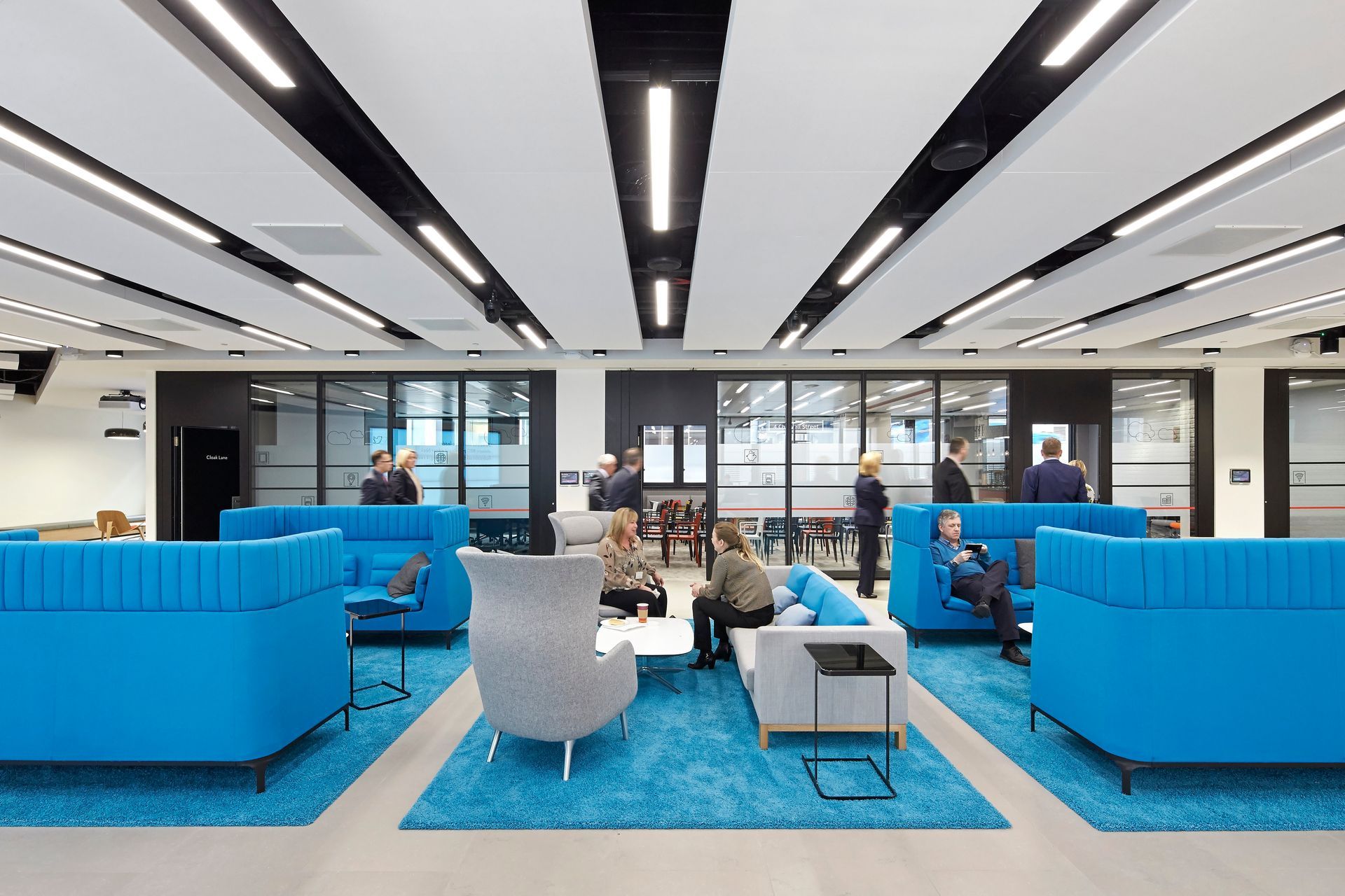 A group of people are sitting on blue couches in a living room.