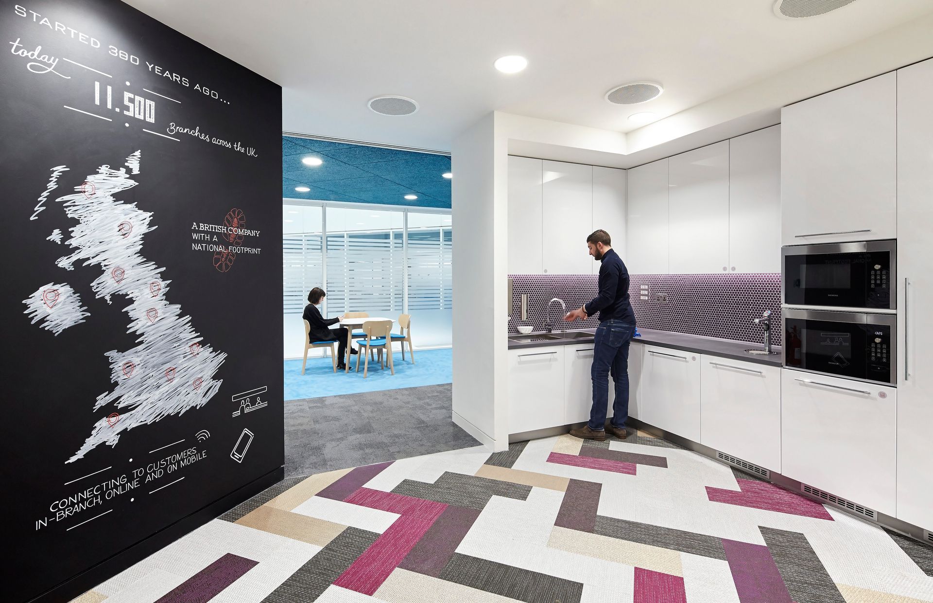 A man is standing in a kitchen with a map of the united kingdom on the wall.