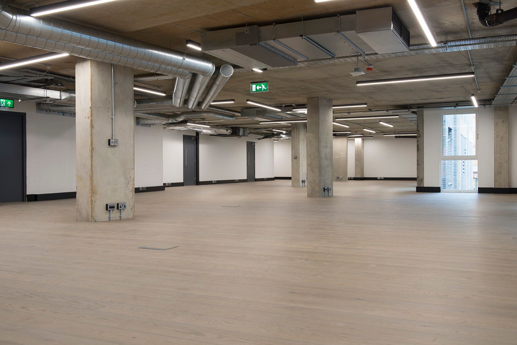 A large empty room with a green exit sign on the ceiling.