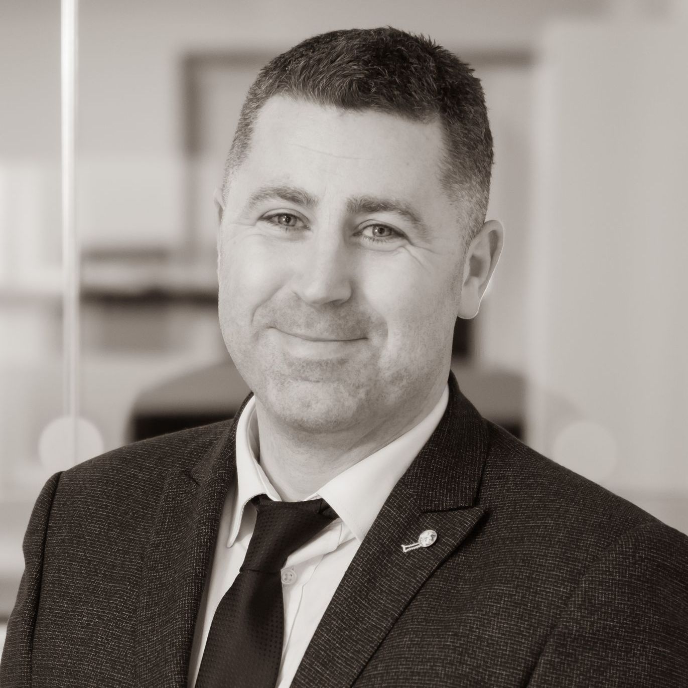 A man in a suit and tie is smiling in a black and white photo.