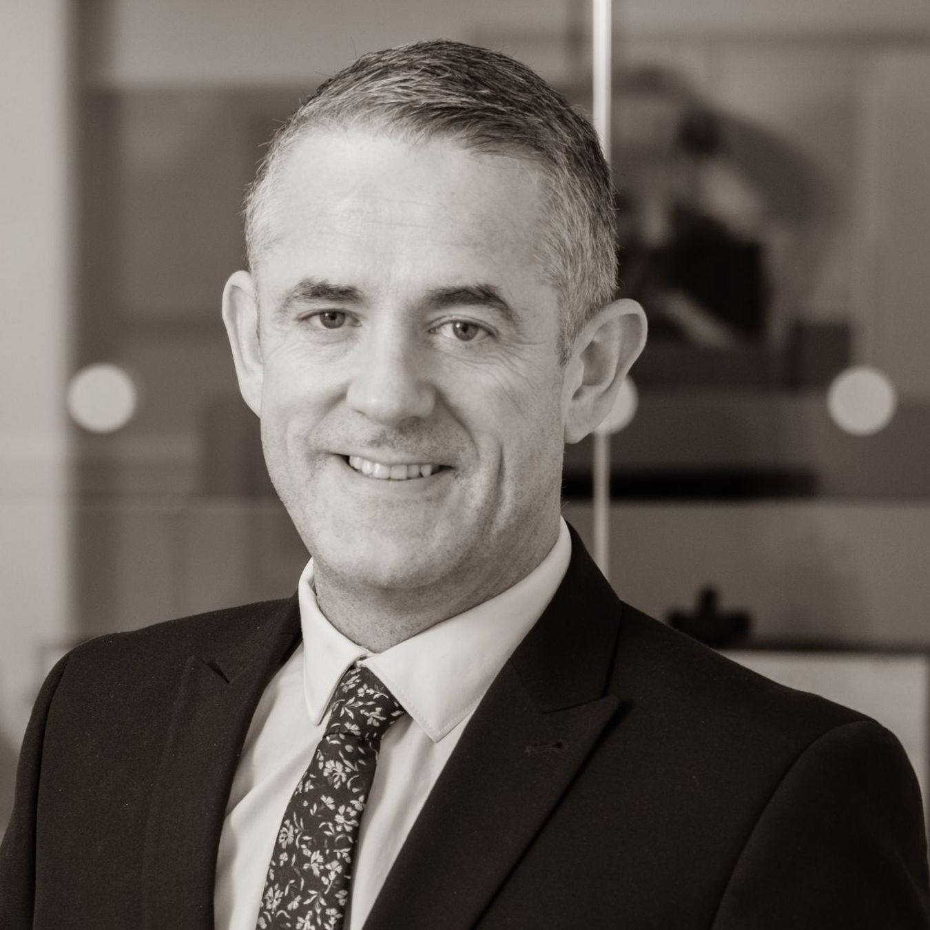 A man in a suit and tie is smiling in a black and white photo.