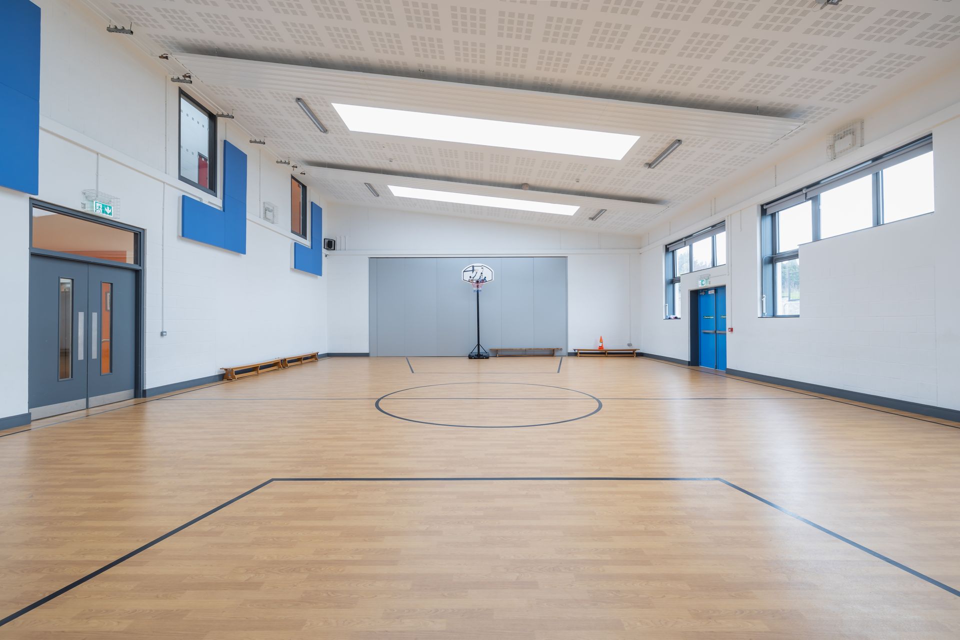 An empty gym with a wooden floor and a basketball hoop.