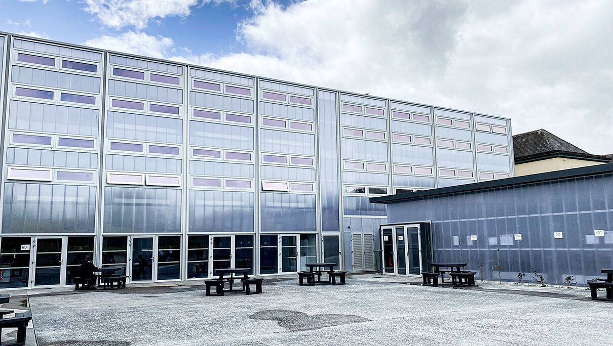 A large building with a lot of windows and picnic tables in front of it.