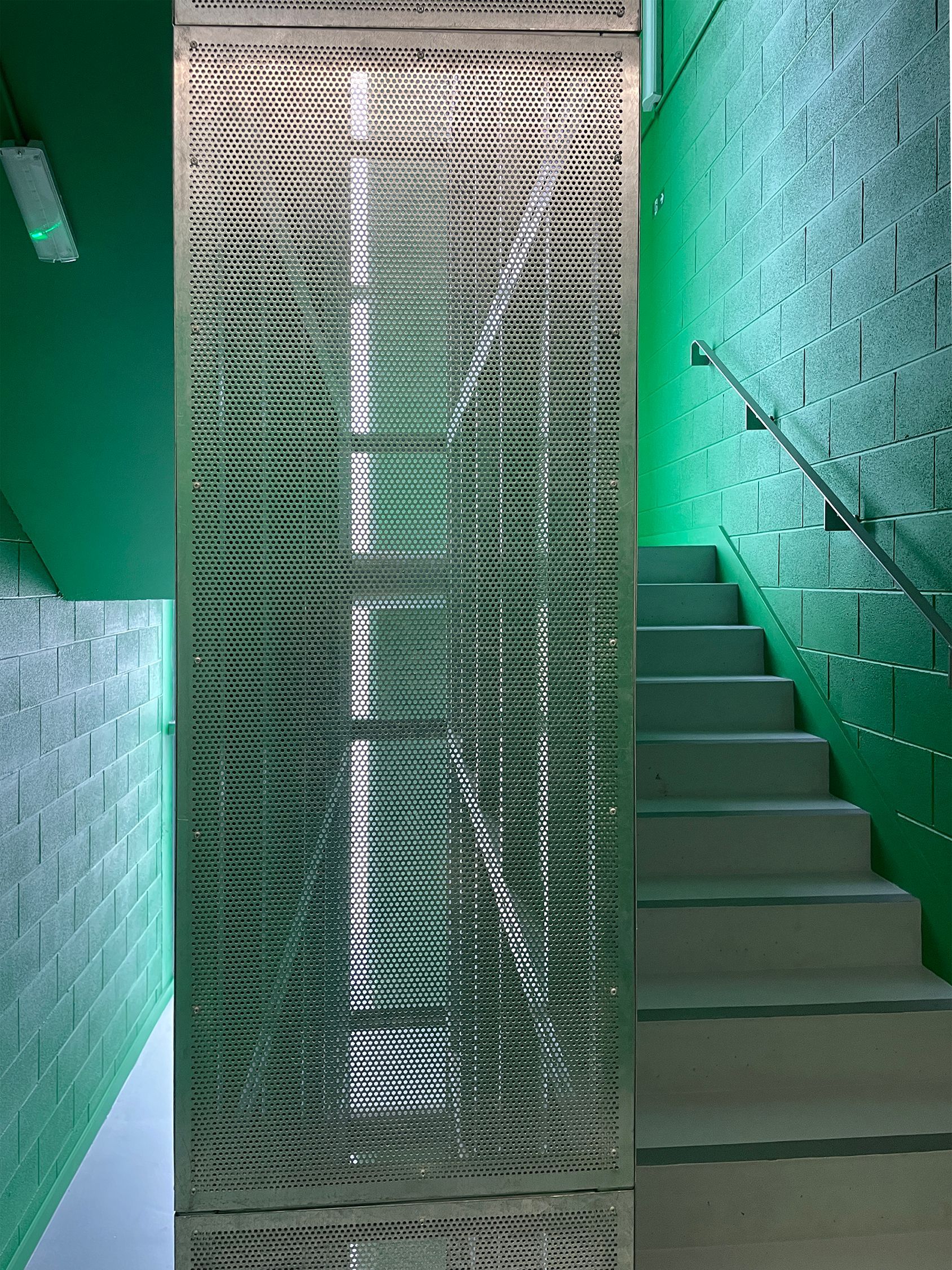 A staircase with a green wall and a metal screen between the stairs.