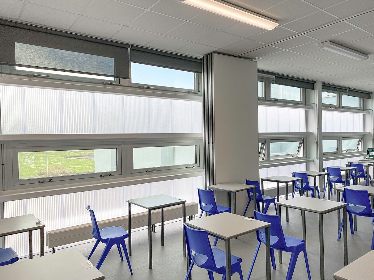 A classroom with tables and chairs and a lot of windows.