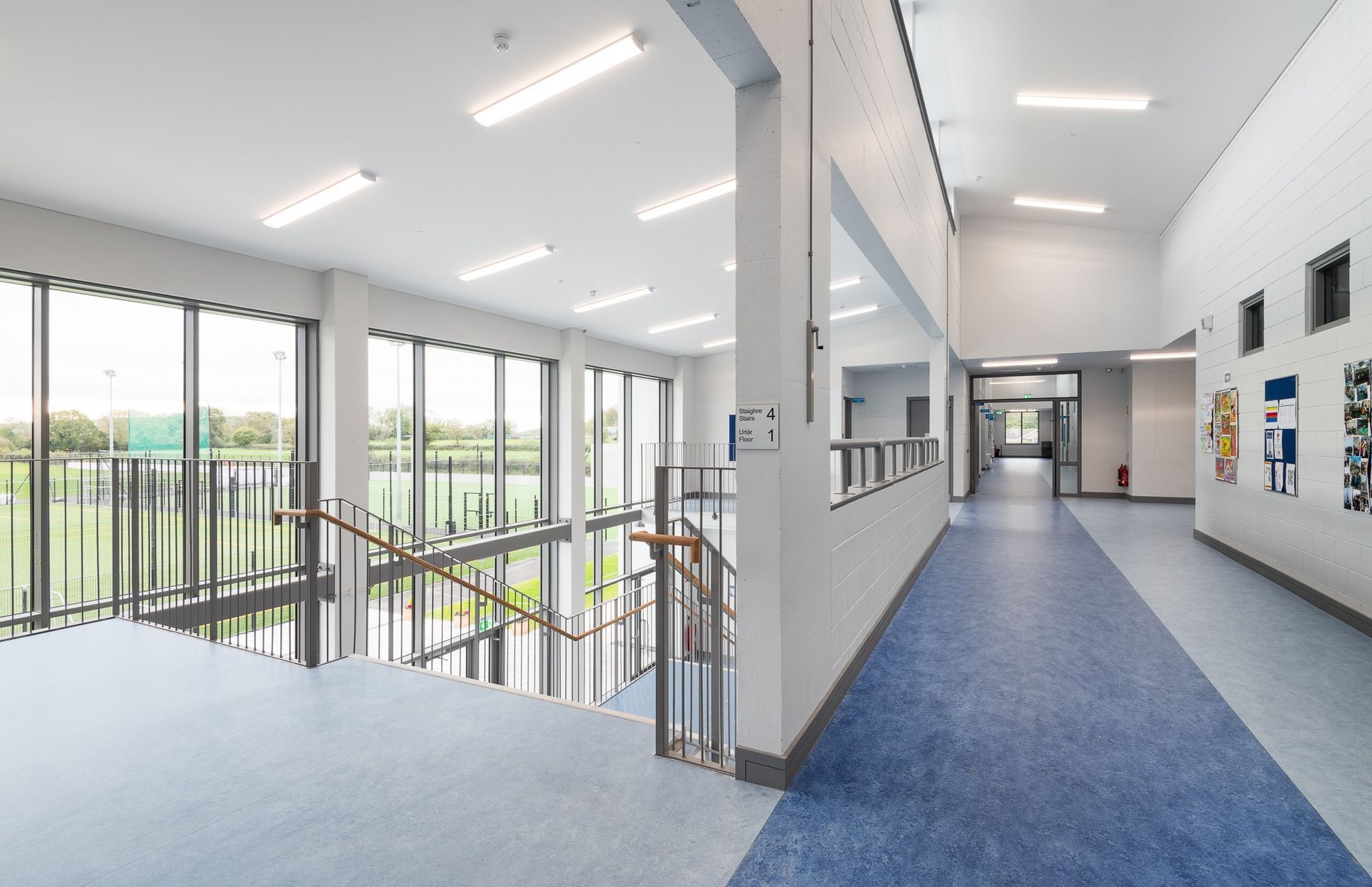 A long hallway with a blue floor and stairs in a school building.