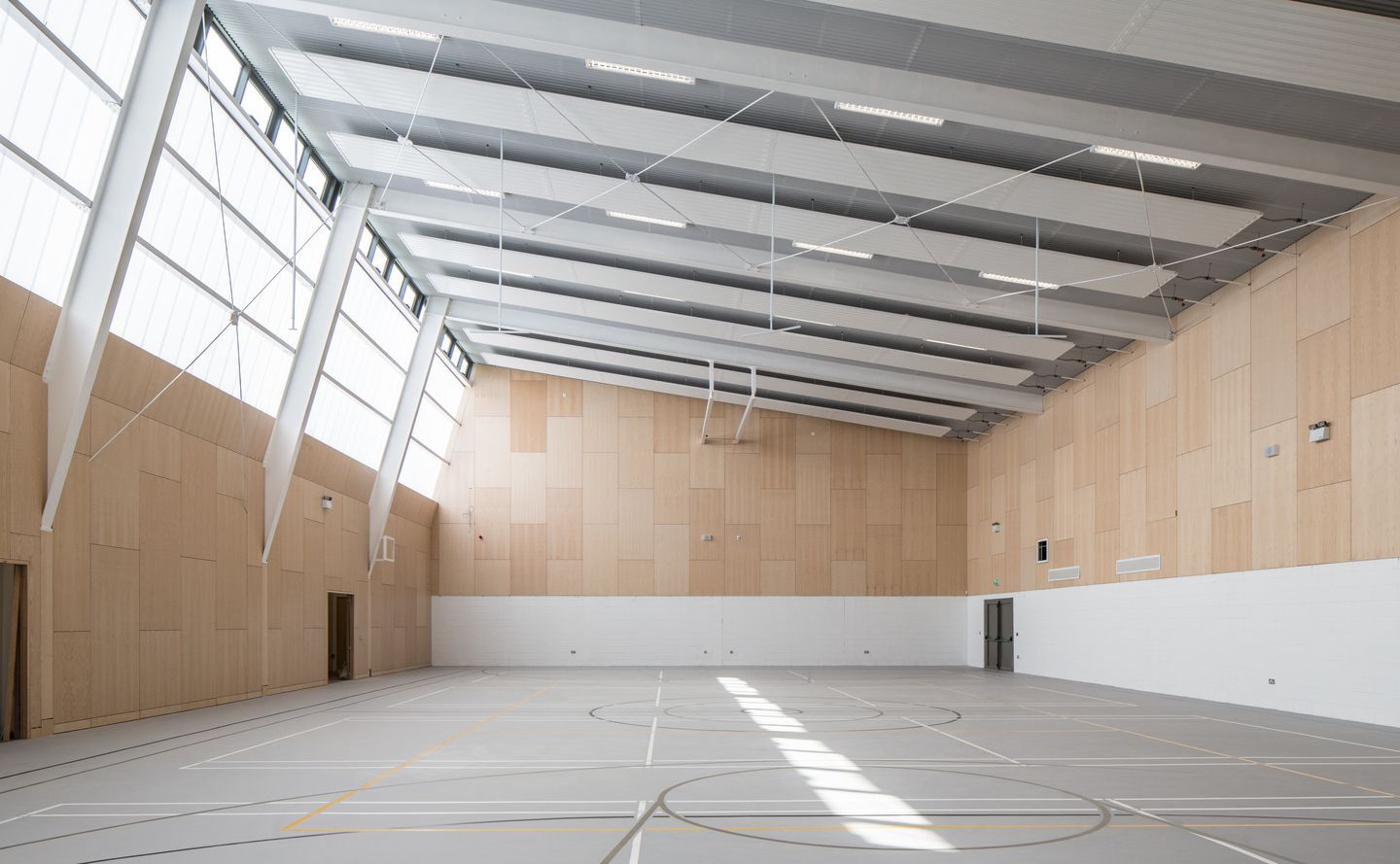 A large empty gym with a wooden ceiling and a basketball hoop.
