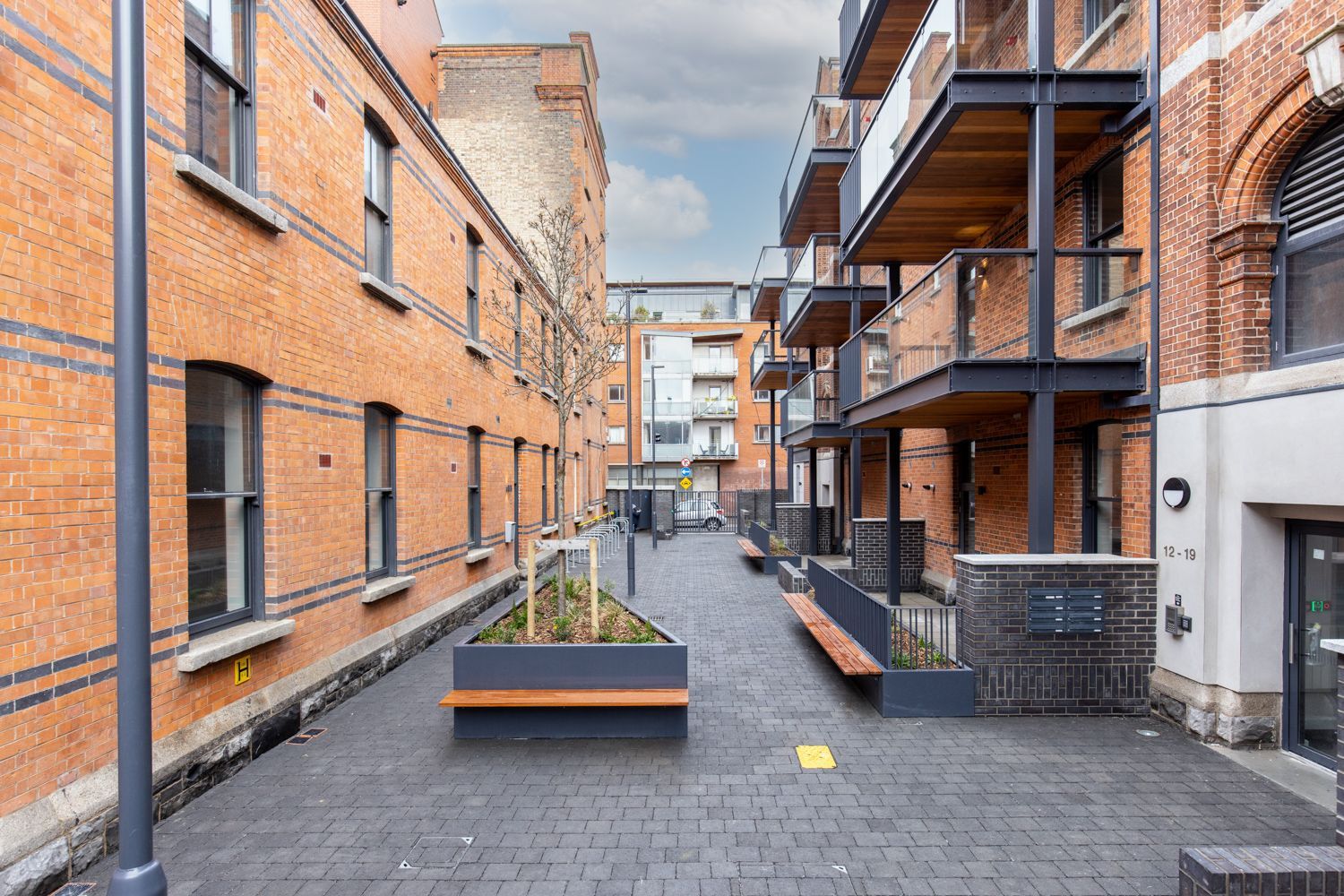 A narrow alleyway between two brick buildings with benches and planters.