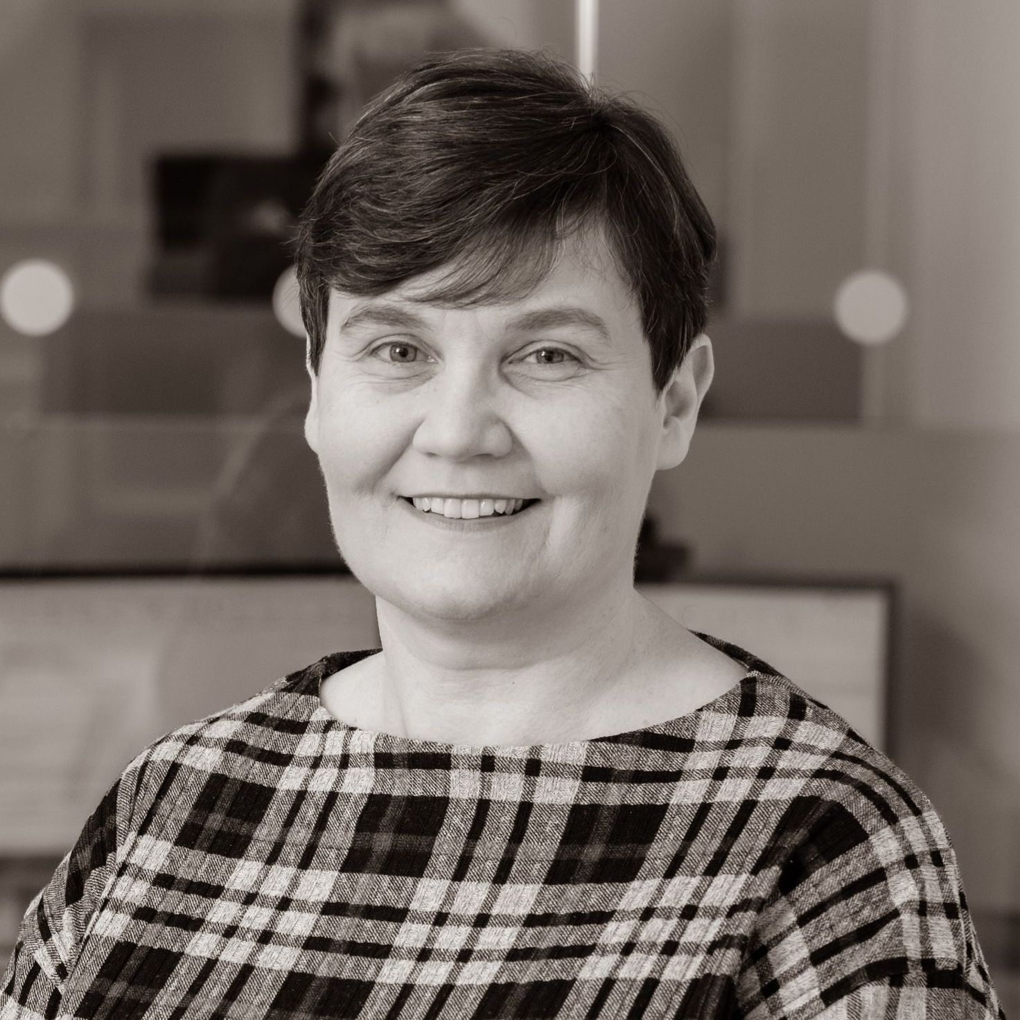 A woman in a plaid shirt is smiling in a black and white photo.