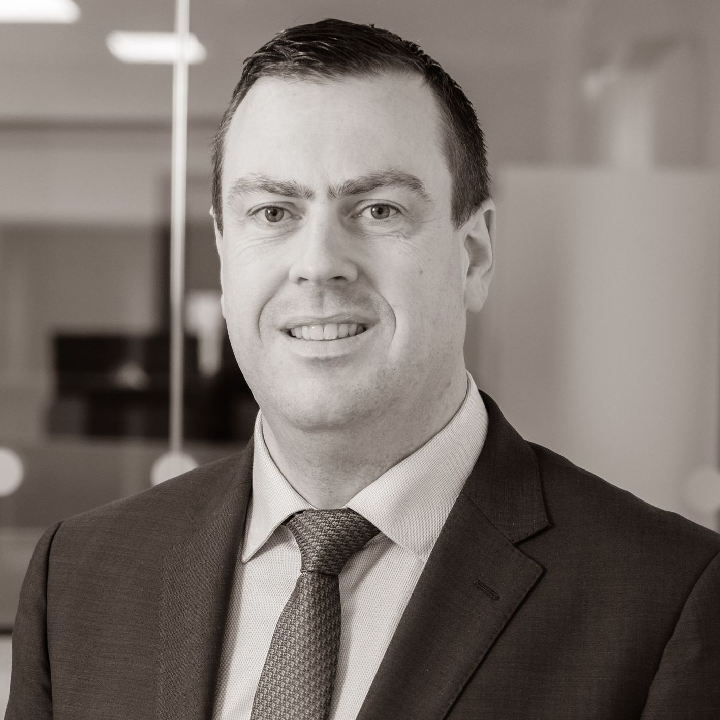 A man in a suit and tie is smiling in a black and white photo.