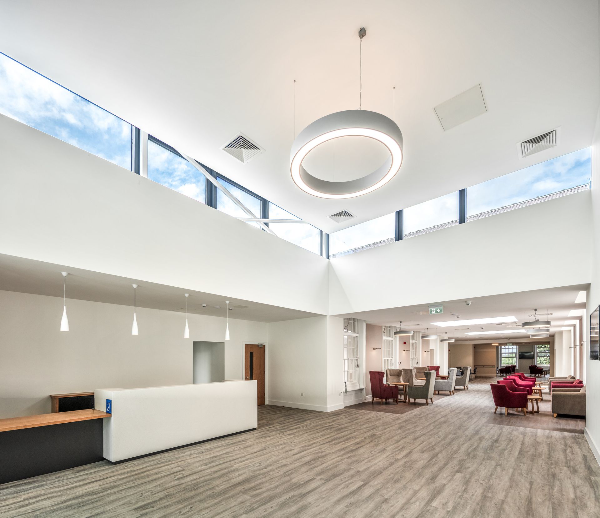 A large lobby with a reception desk , chairs , tables and a ceiling light.