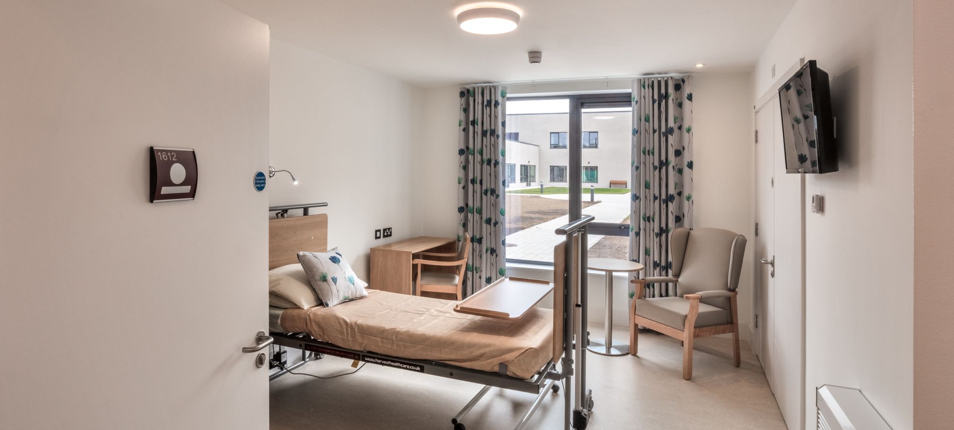 A hospital room with a bed , chair , table and television.