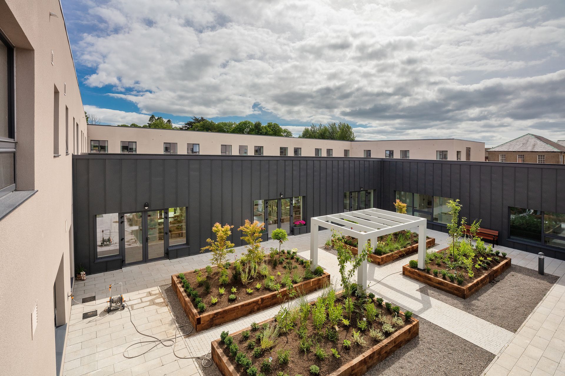 A courtyard with a pergola and planters in front of a building.