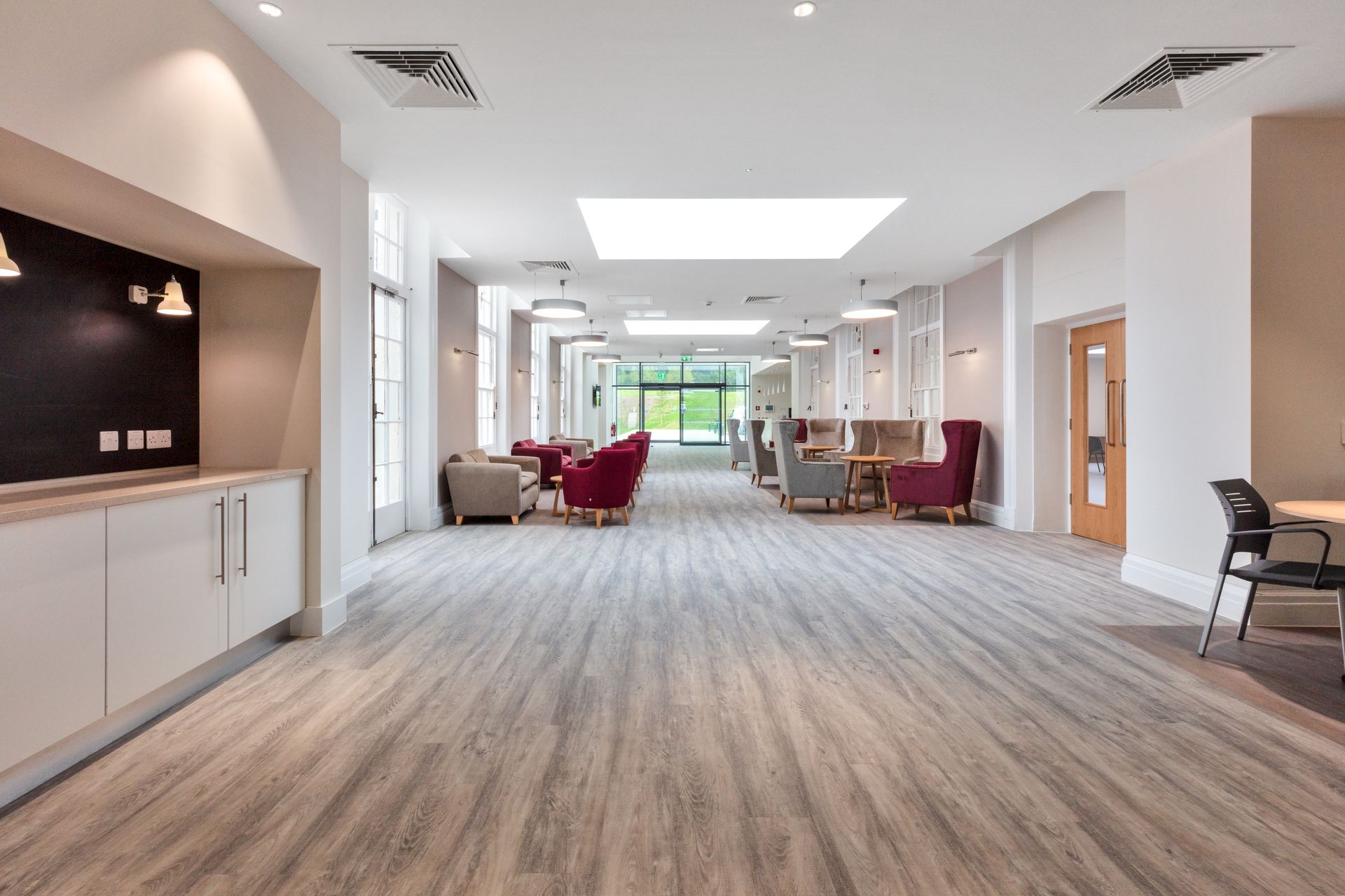 A long hallway with wooden floors and chairs in a building.