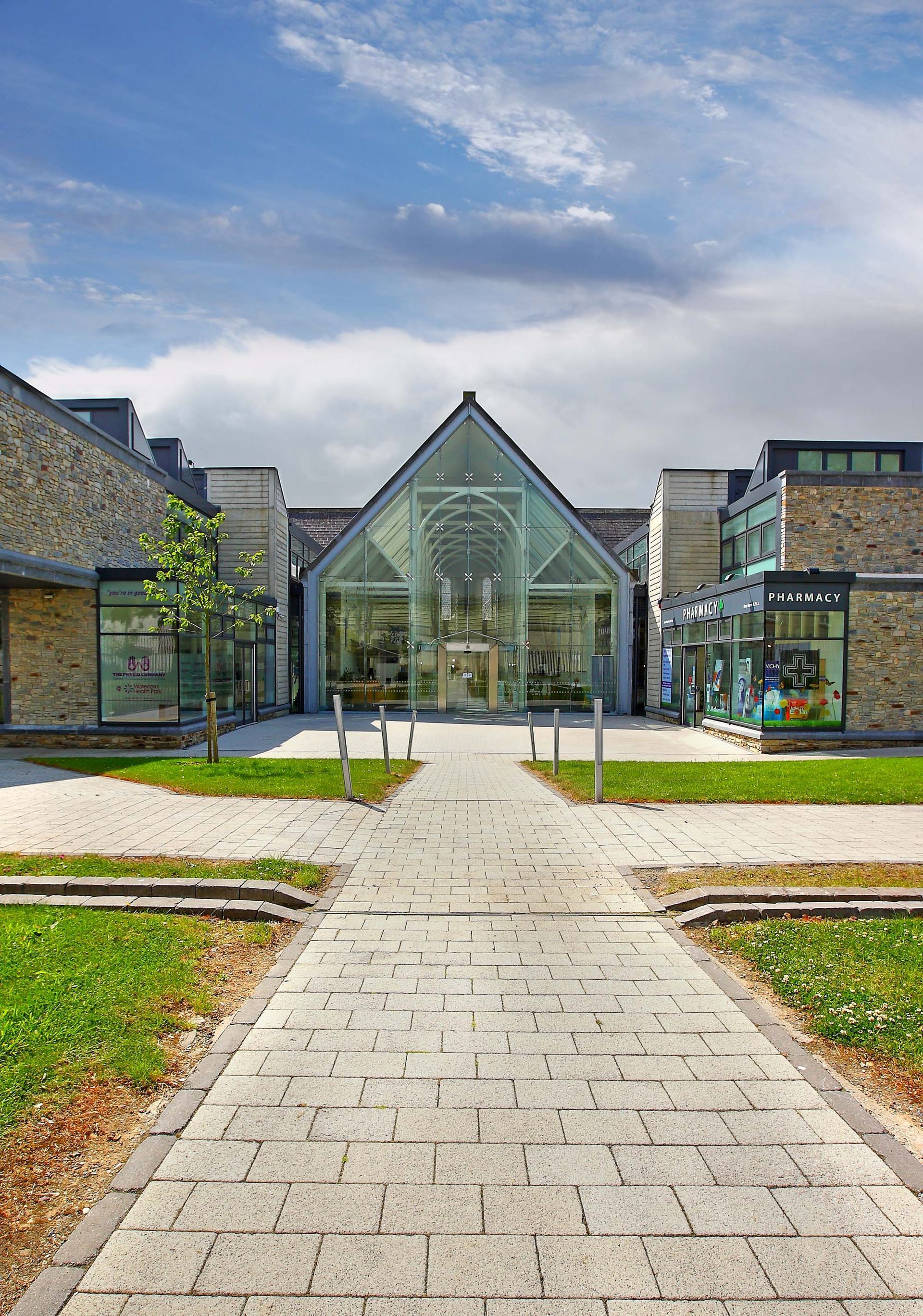A brick walkway leading to a large building with a glass facade.