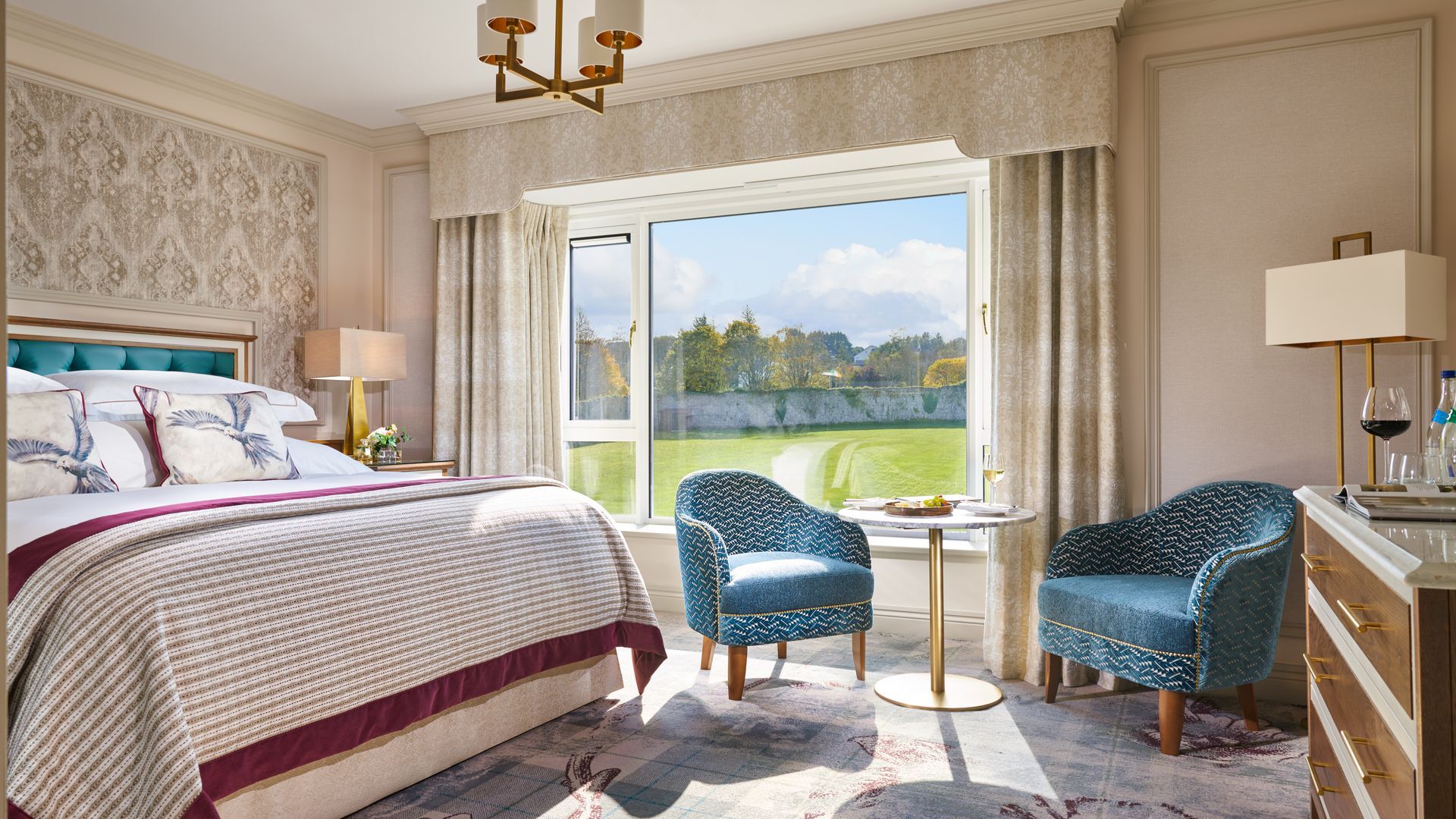 A hotel room with a king size bed , two chairs , a table and a large window.