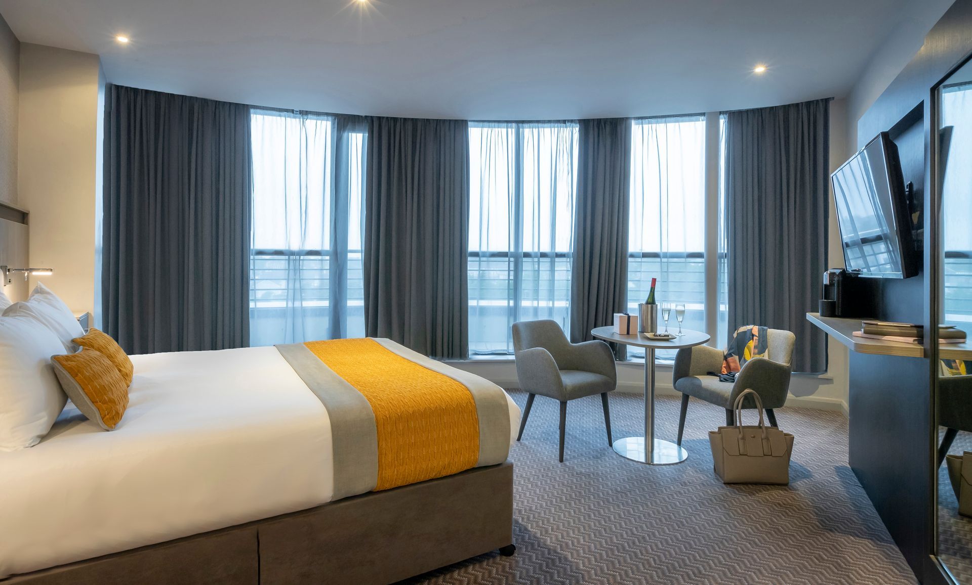A hotel room with a king size bed , chairs , table and television.