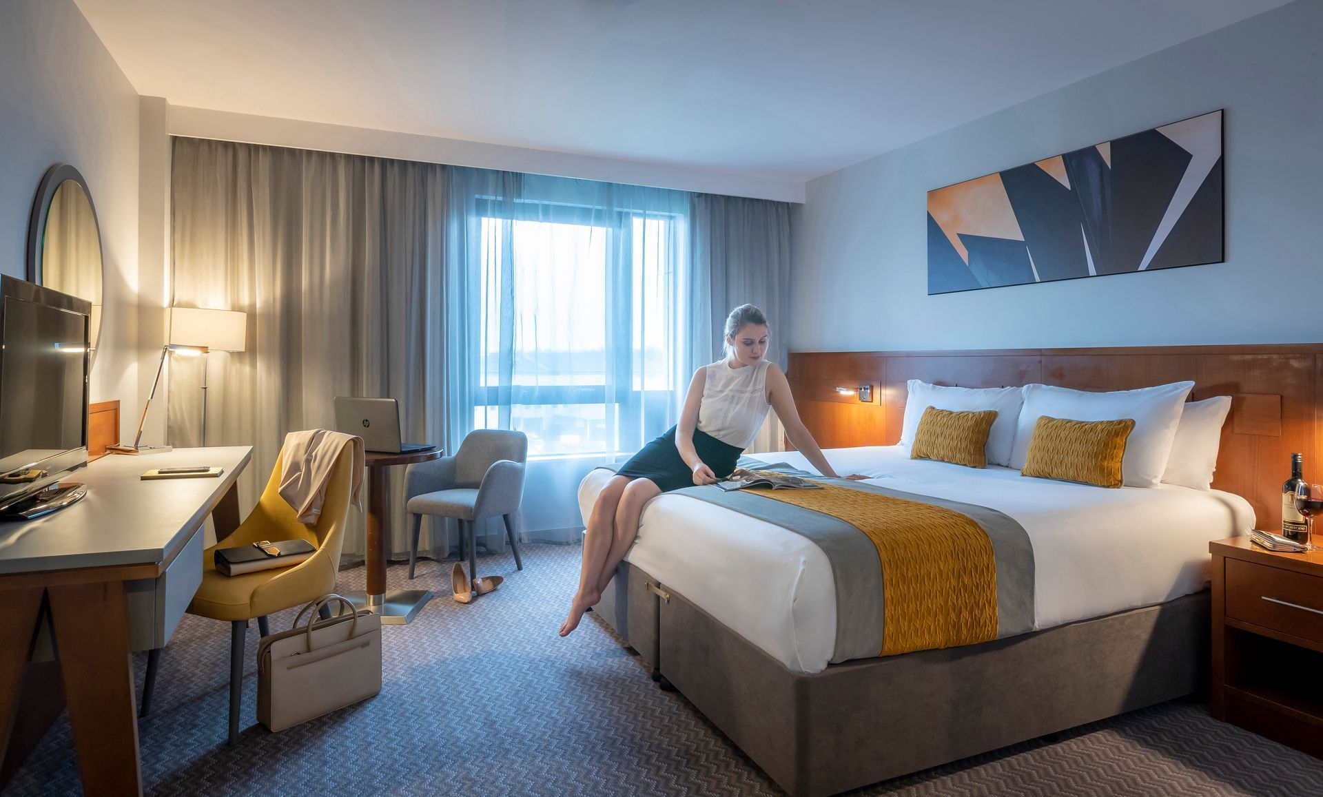 A woman is sitting on a bed in a hotel room.