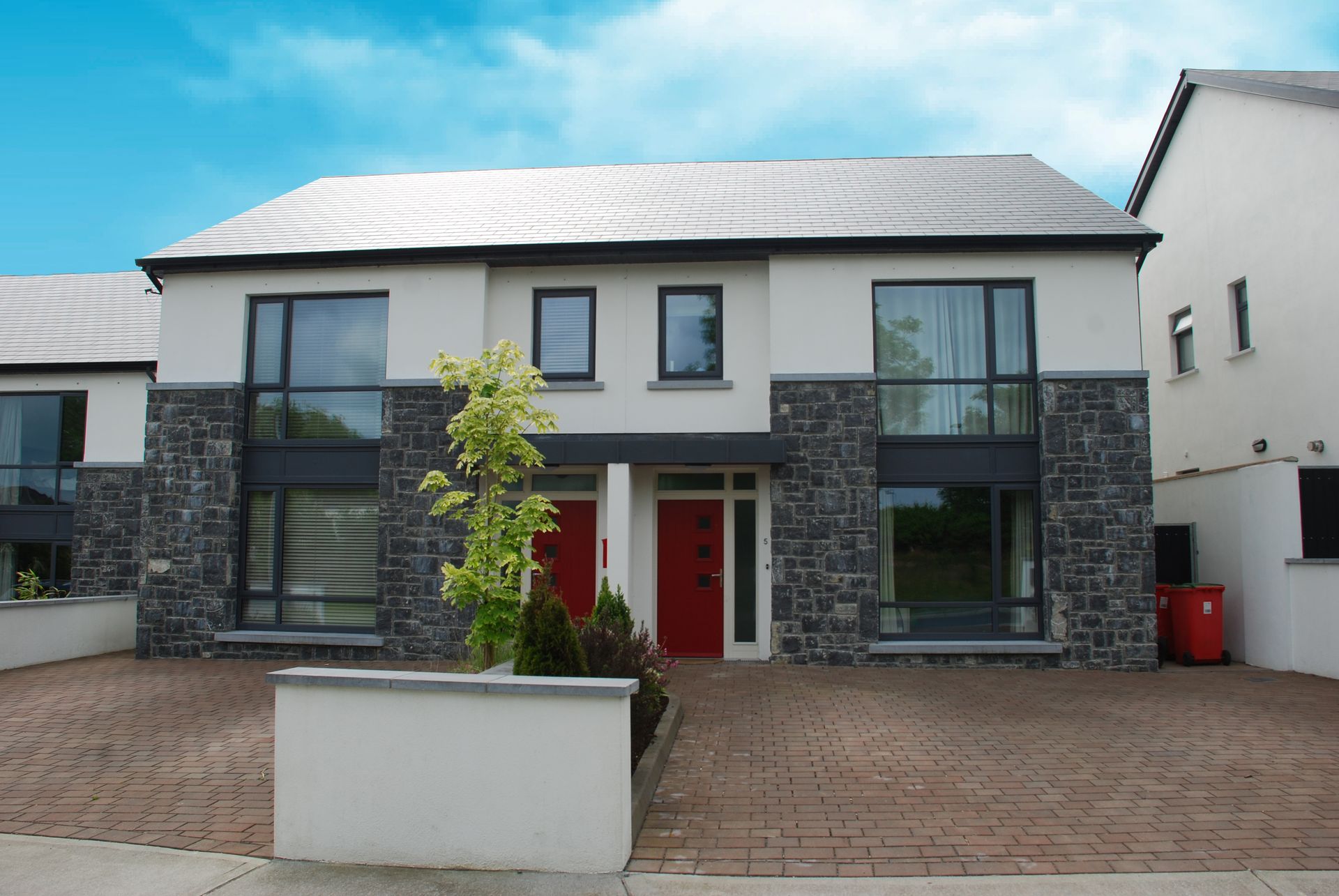 A large white house with a red door and a brick driveway