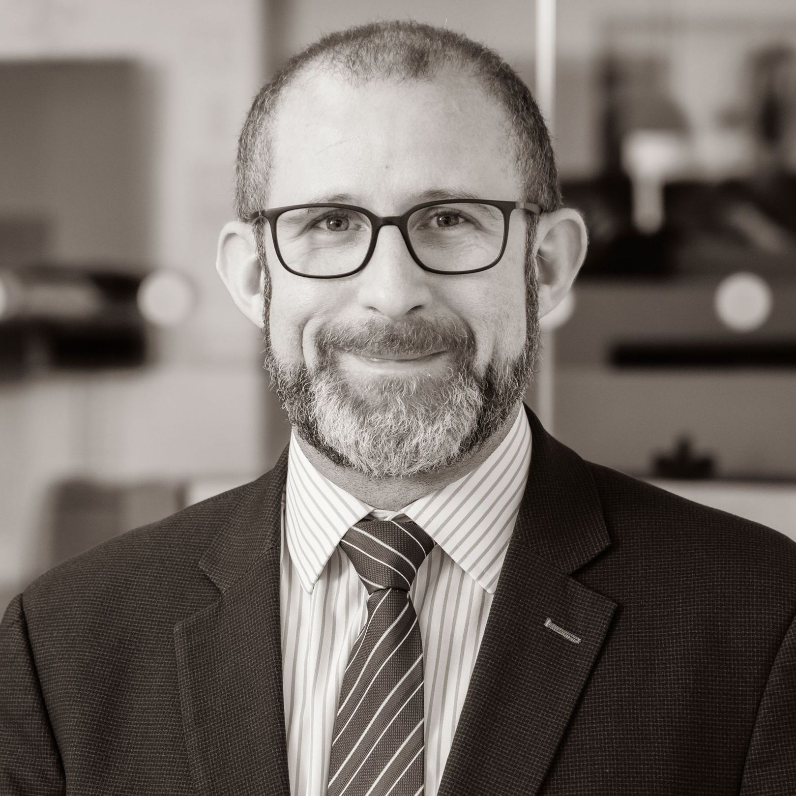 A man with a beard and glasses is wearing a suit and tie.