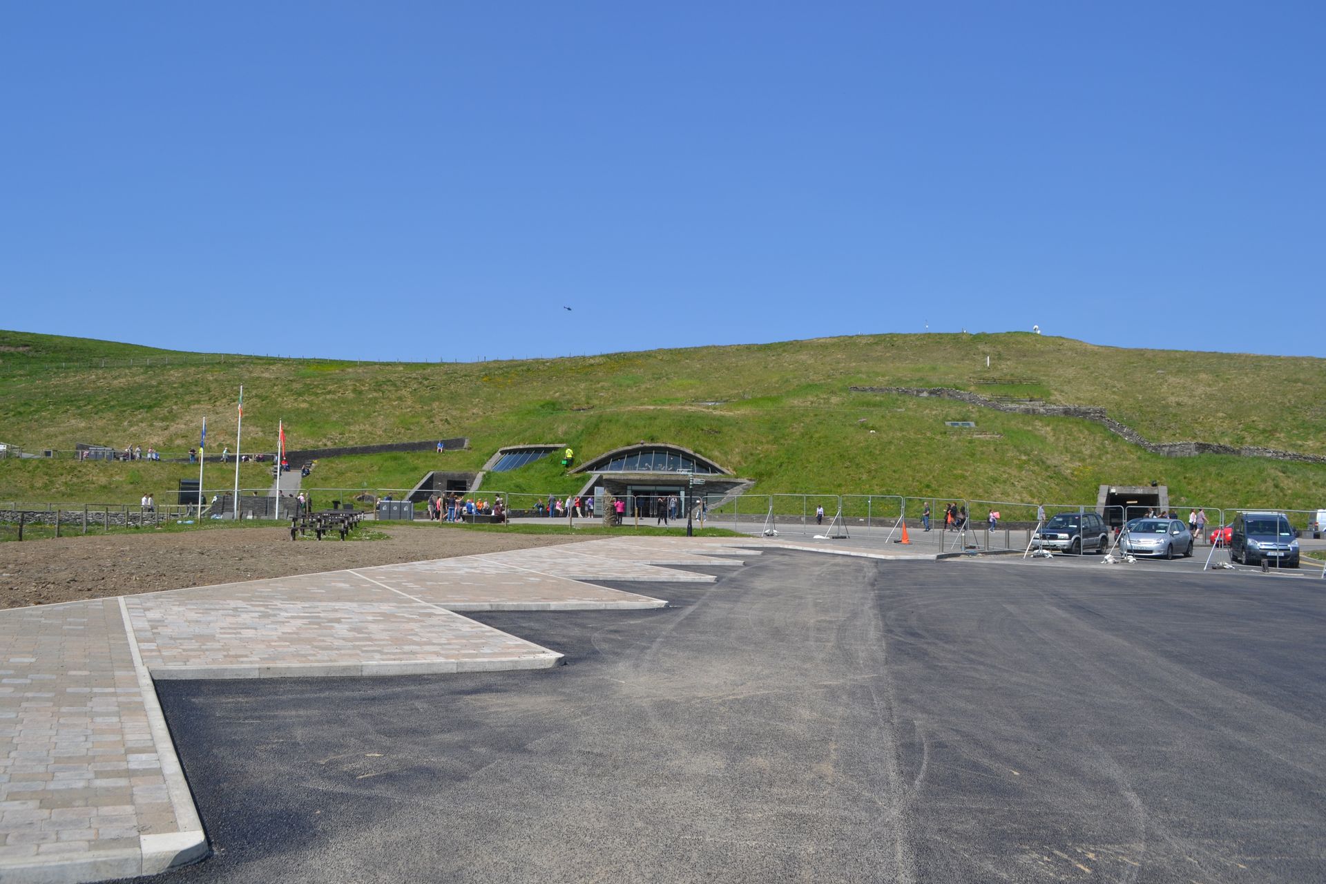 A parking lot with cars parked in front of a grassy hill.