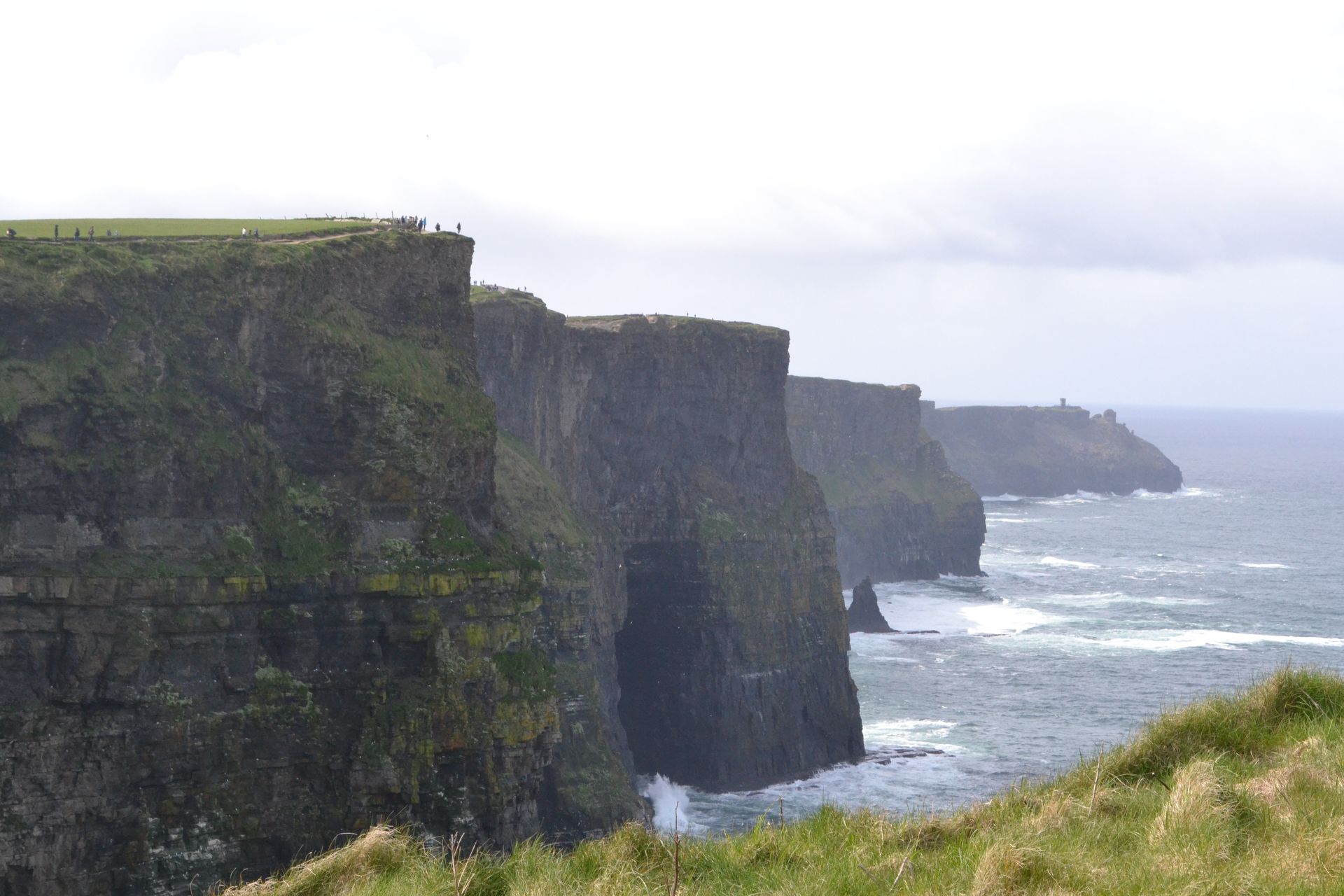A cliff overlooking the ocean with a grassy hill in the foreground.