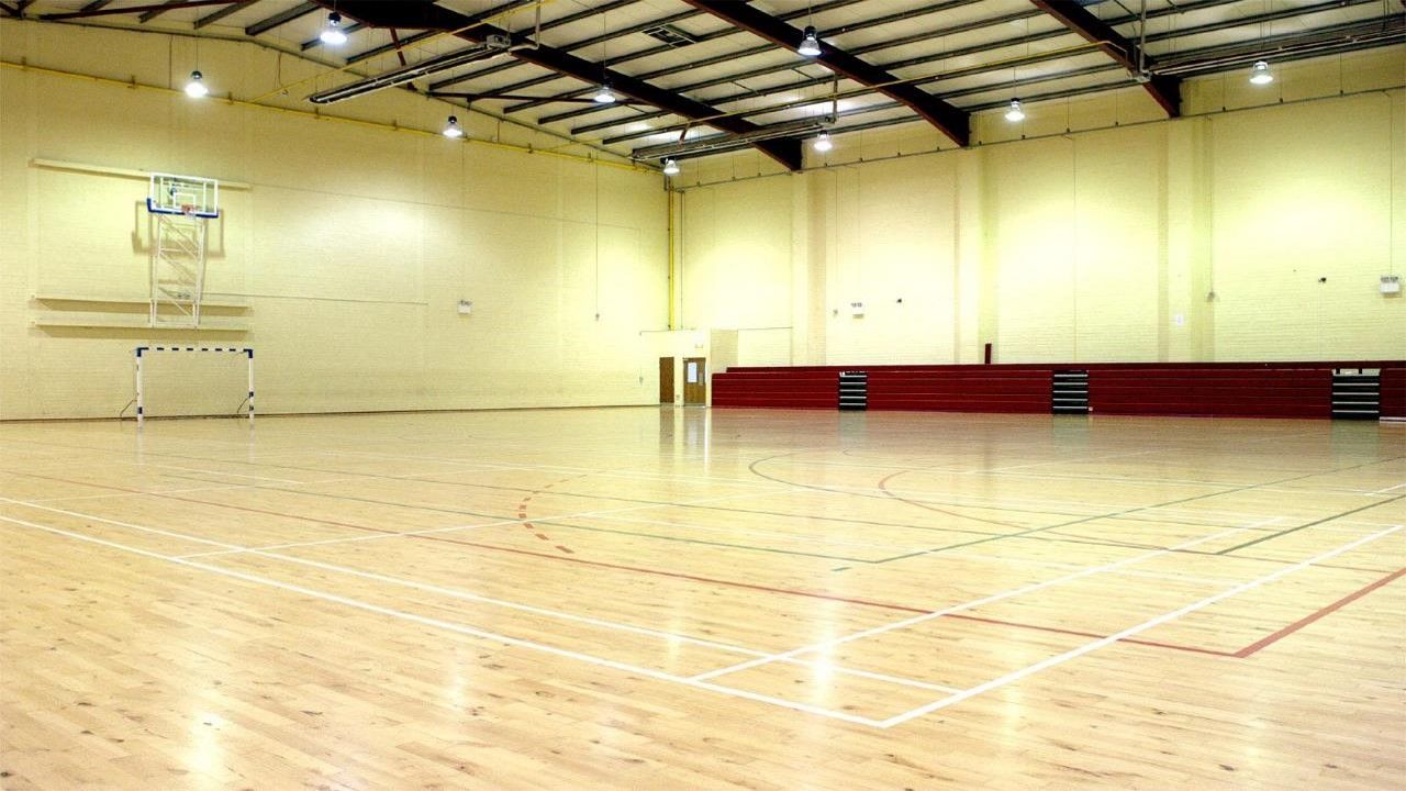 An empty gym with a wooden floor and a basketball hoop.