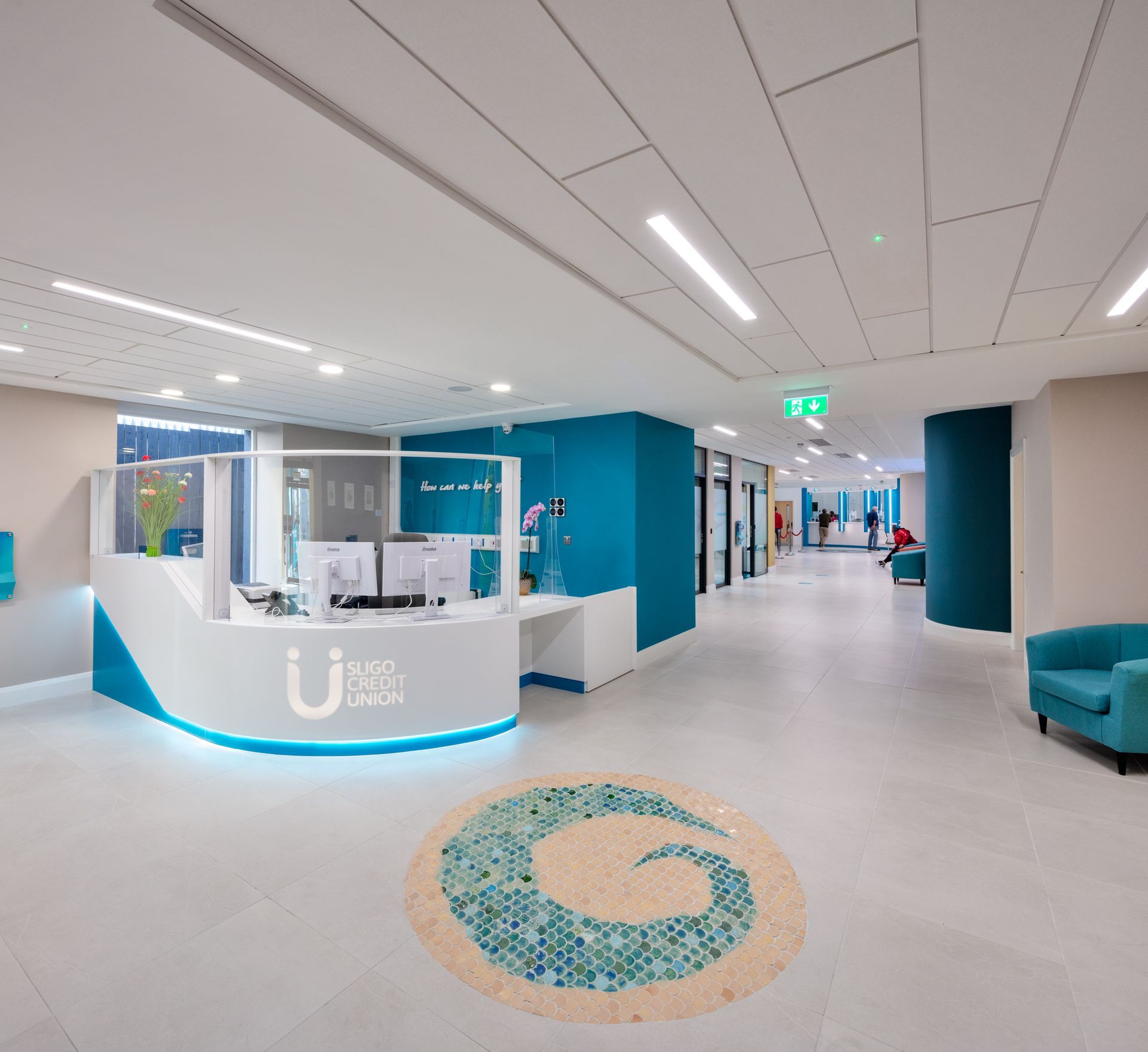 A hospital lobby with a blue chair and a white counter with the letter u on it