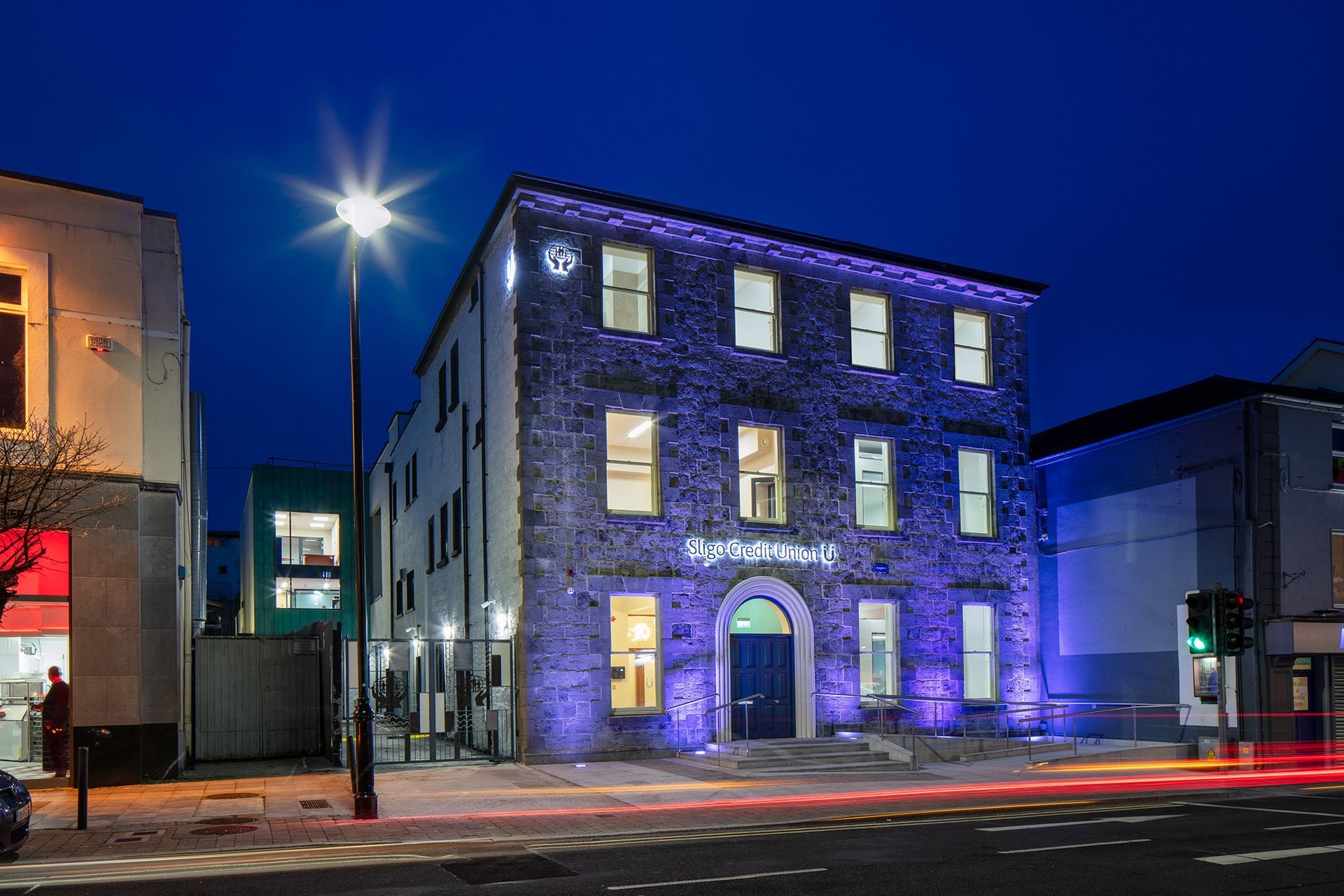 A large stone building is lit up with purple lights at night.