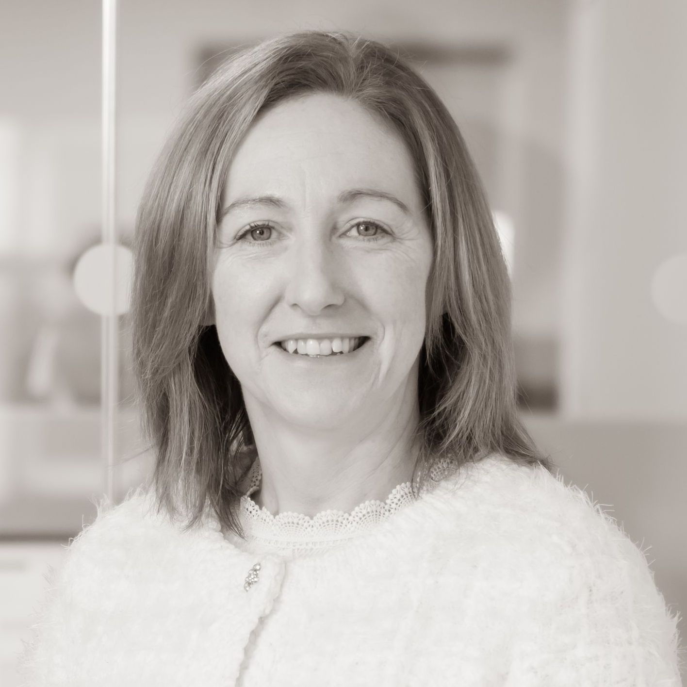 A woman in a white sweater is smiling in a black and white photo.