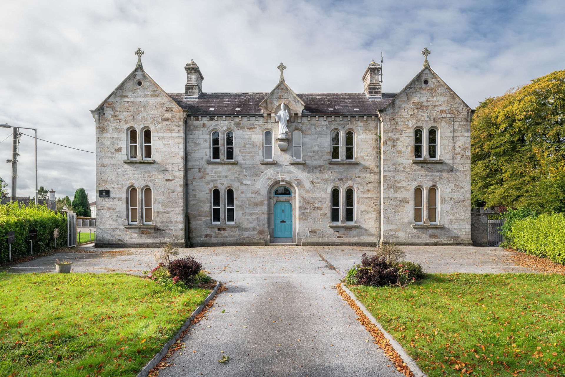 A large stone building with a blue door is surrounded by grass and trees.