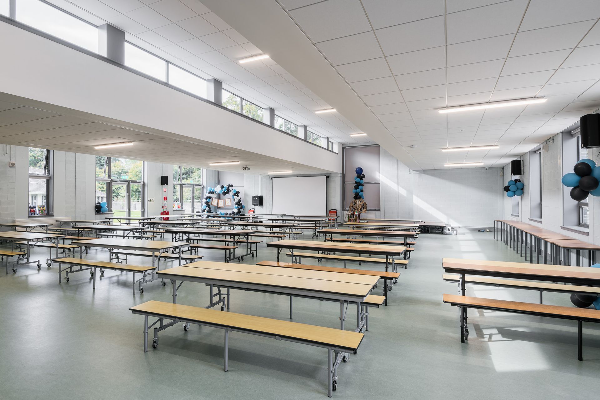 A large room filled with tables and benches in a school cafeteria.