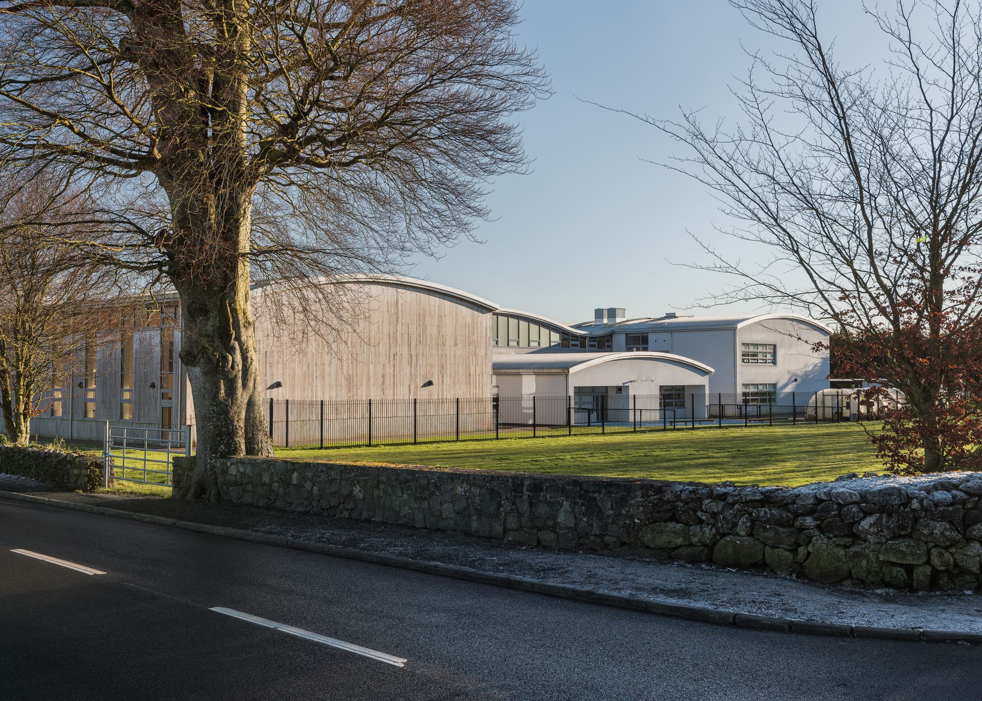 A large white building is sitting on the side of a road next to a stone wall.