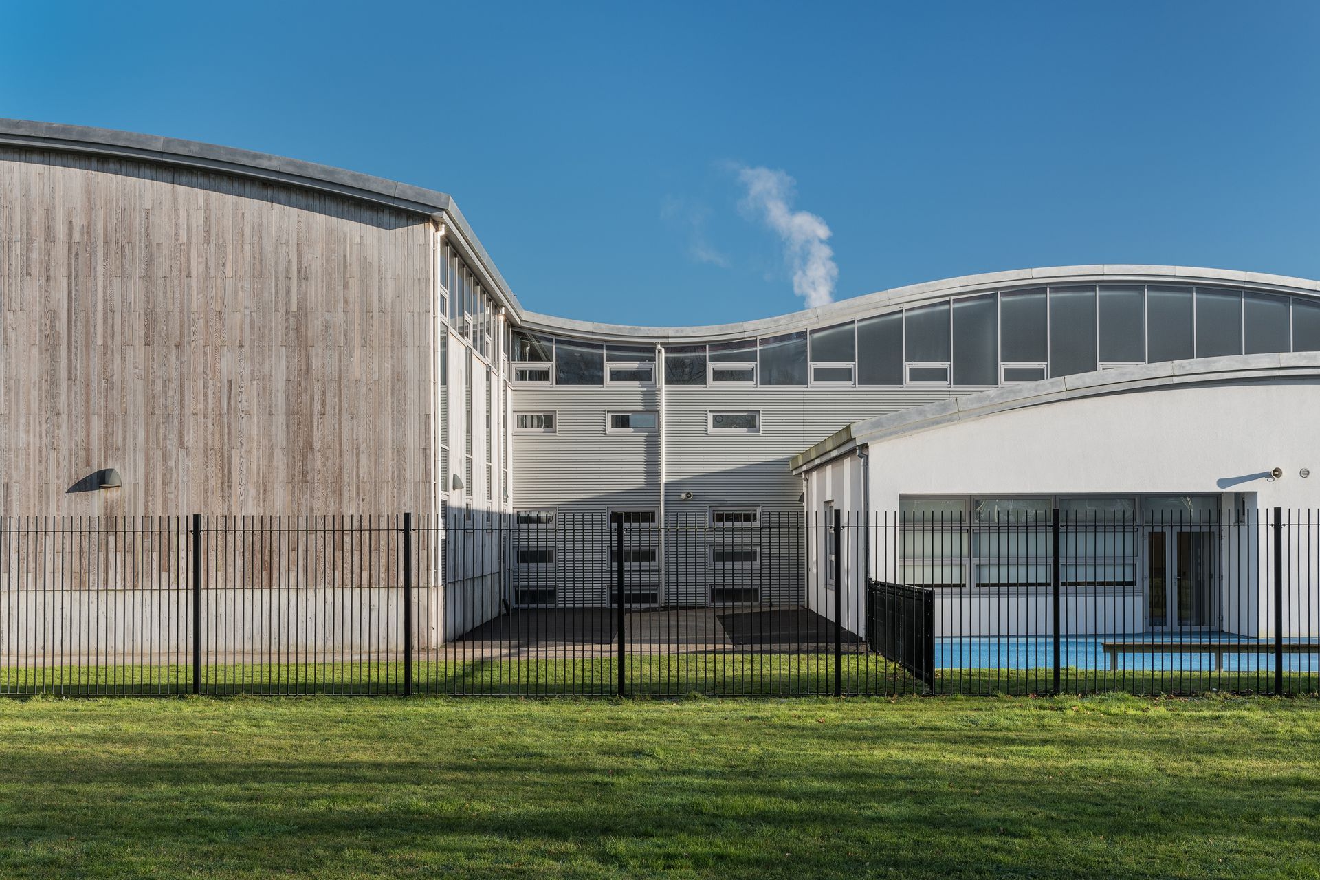 A large white building with a fence around it and a pool in front of it.