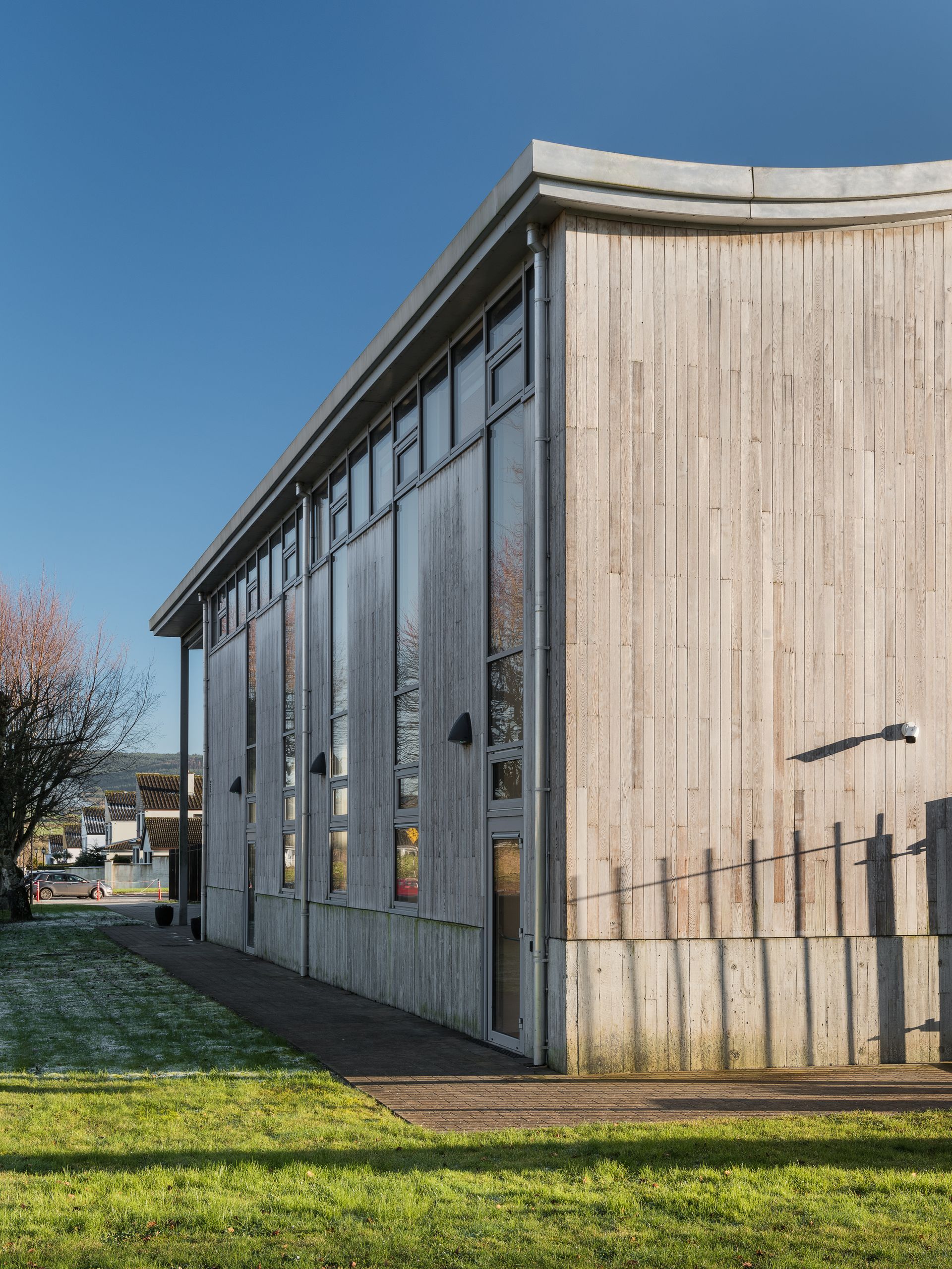 A large wooden building with a lot of windows is sitting on top of a lush green field.