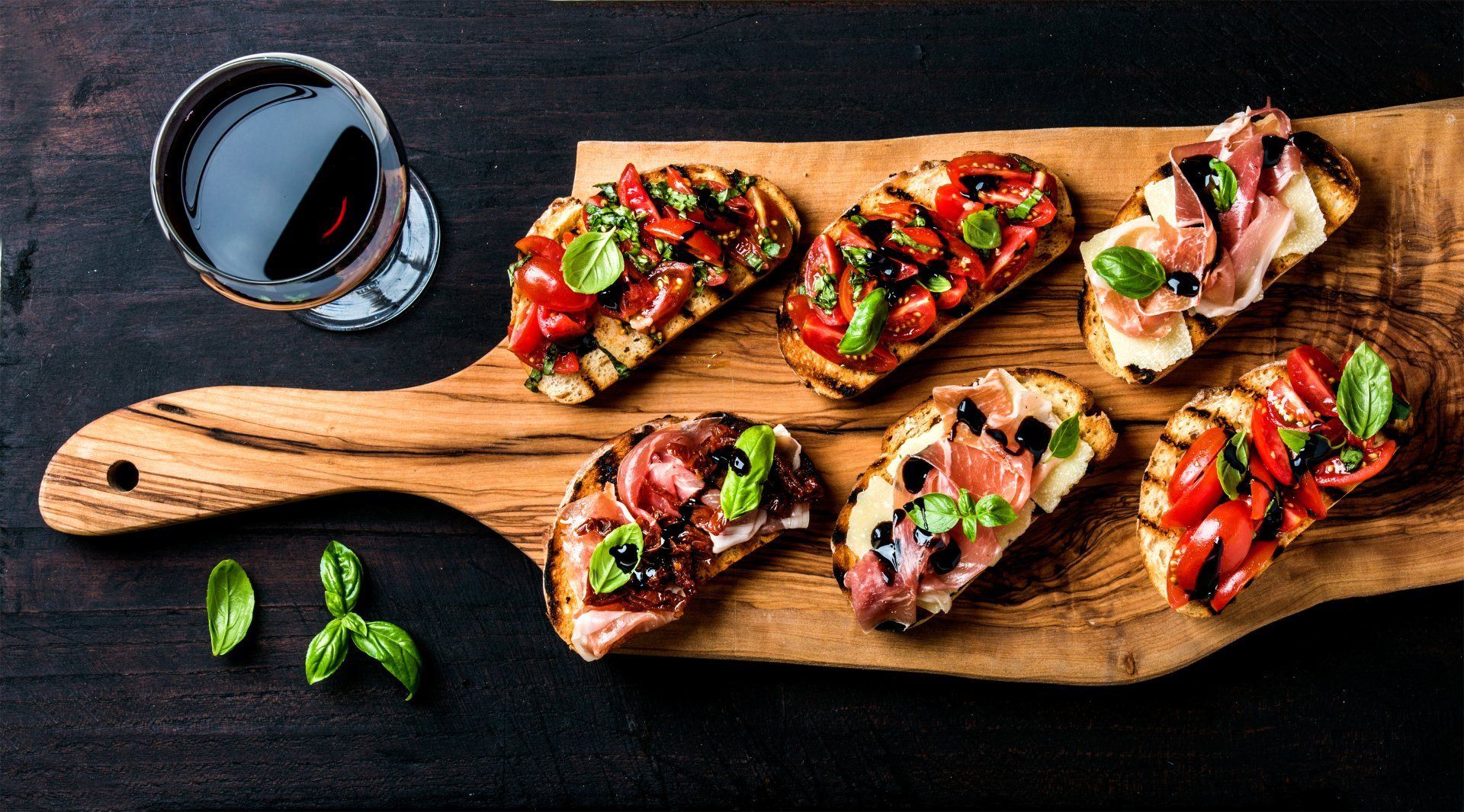 A wooden cutting board topped with sandwiches and a glass of wine.