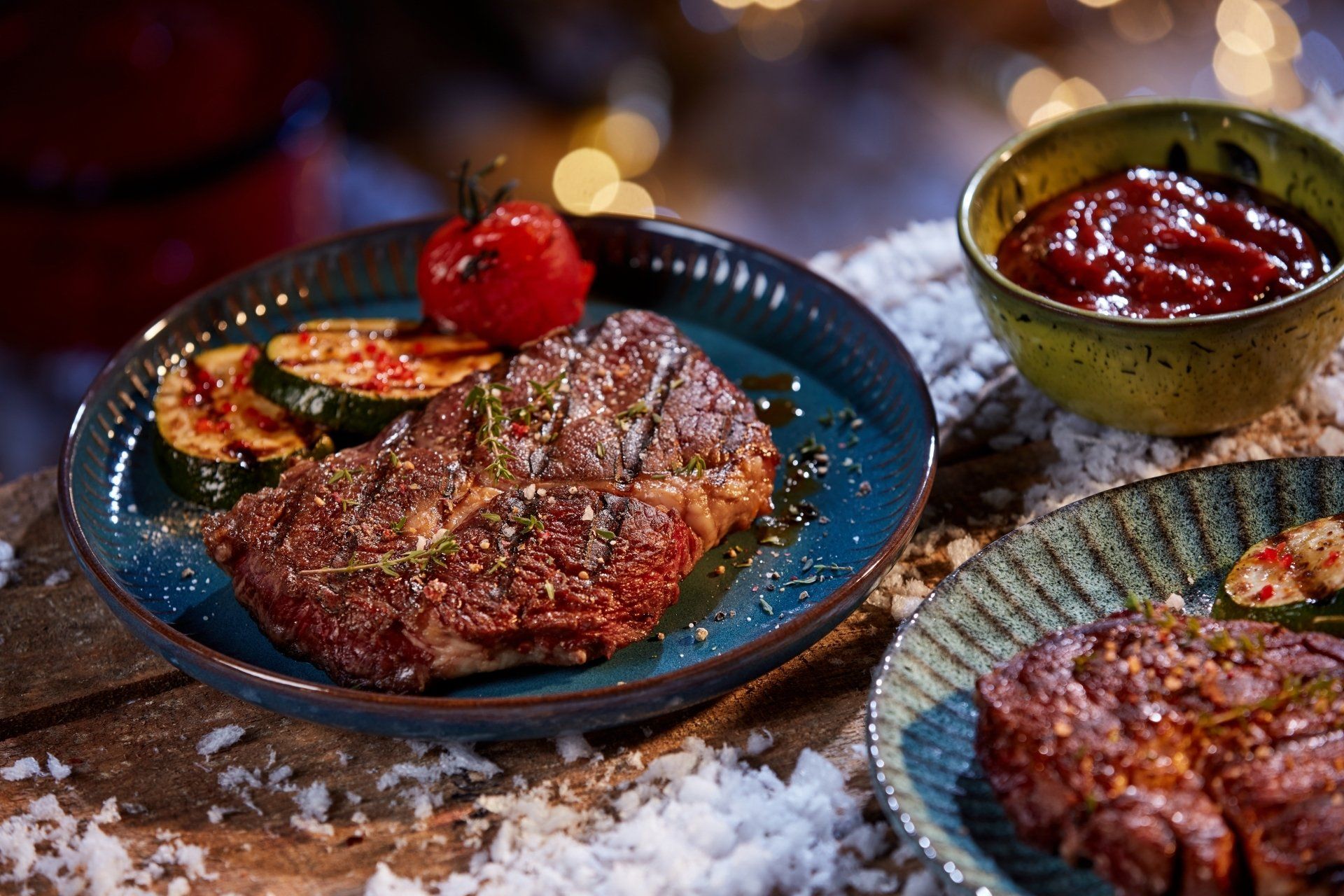 A plate of steak and vegetables on a table with a bowl of sauce.