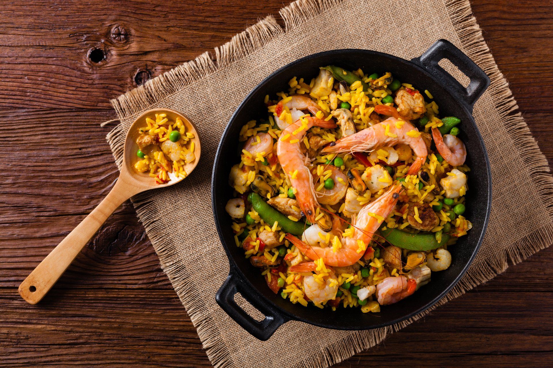 A pan of shrimp and rice with a wooden spoon on a wooden table.