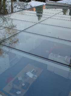 Panneau de toit en verre avec vue sur une pièce, lumière réfléchie et arbres enneigés au-dessus.