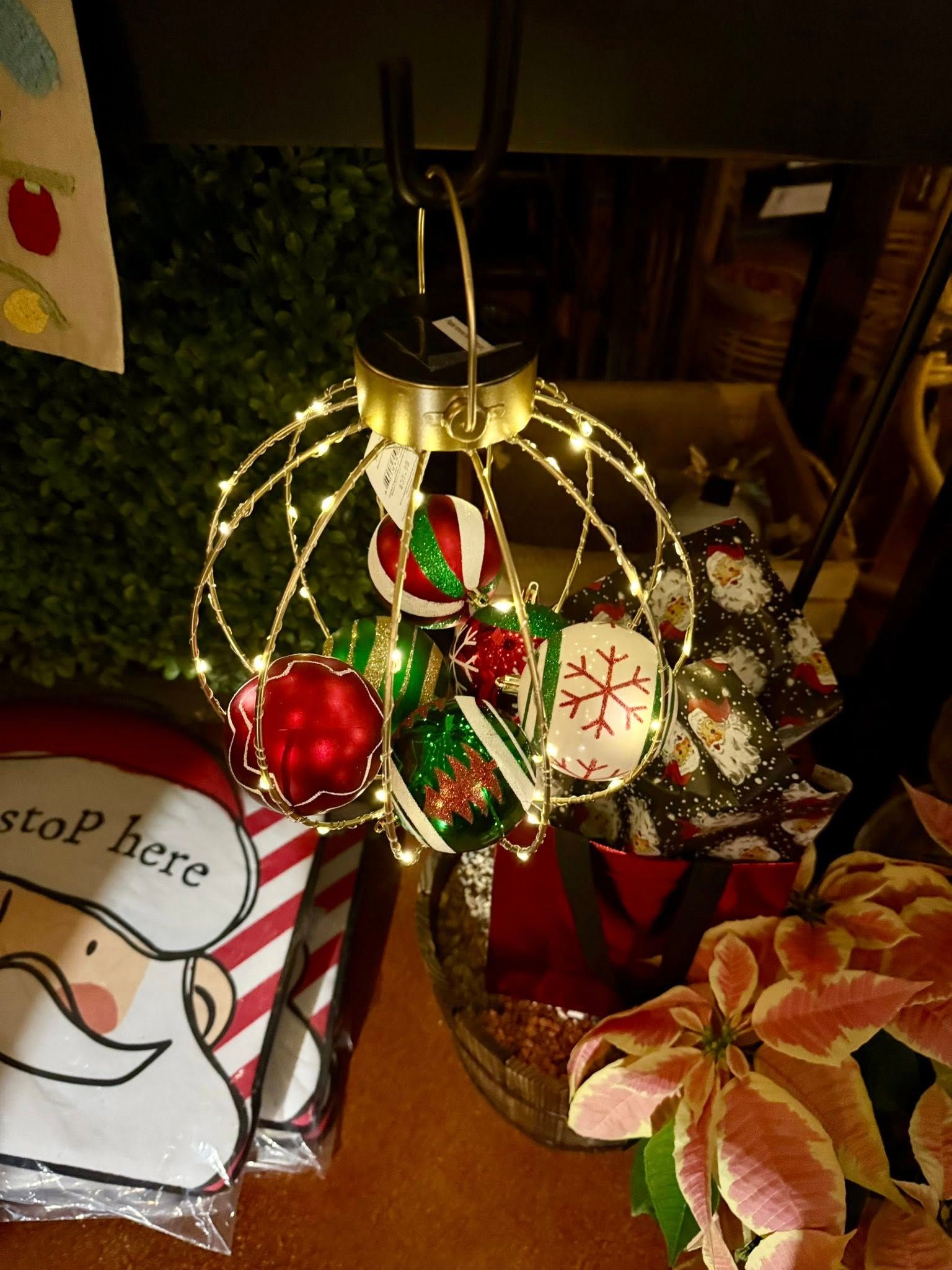 A gold wire-frame ornament filled with multi-colored glass baubles and illuminated by small white fairy lights.
